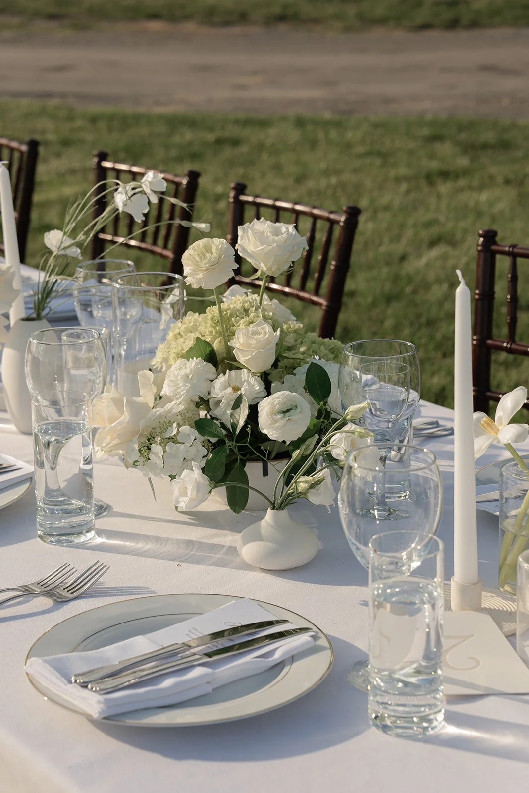 Outdoor wedding place setting with ivory flowers and clear glassware overlooking the Hayfield at Goodstone Inn.