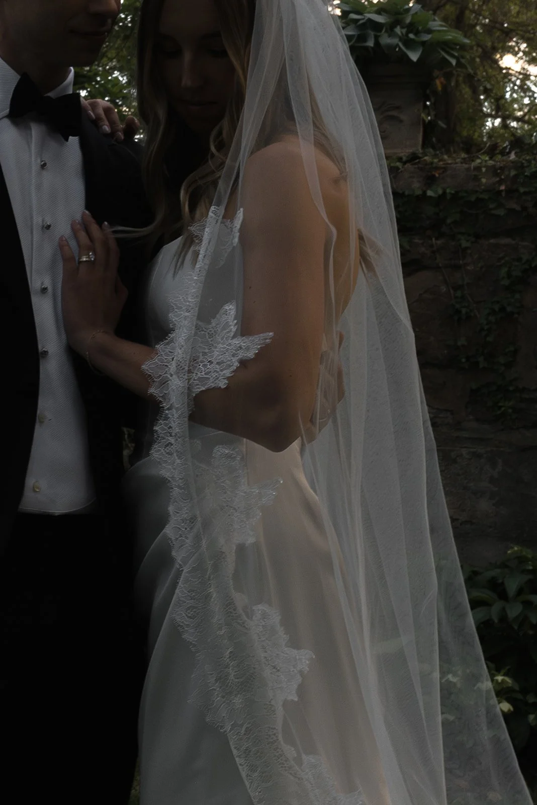 Bride and groom embracing beneath the bride’s sheer cathedral veil in the gardens at Goodstone Inn.