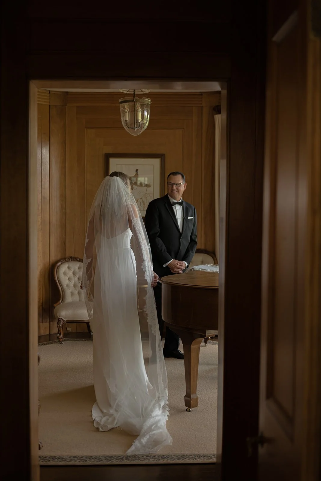 Bride moving through a softly lit interior room in her wedding gown at Goodstone Inn to meet her father for a first look moment. 