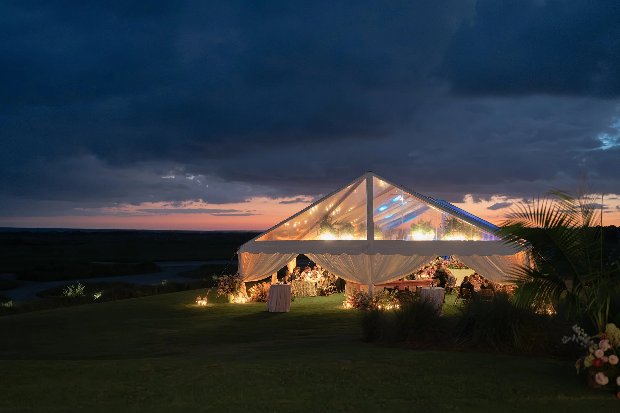 Clear-top wedding reception tent glows beneath a dramatic blue-hour sky at The Ocean Course on Kiawah Island.