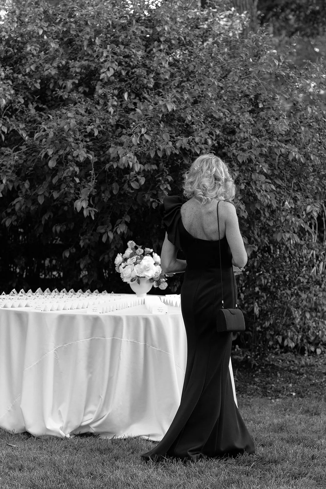 Black-and-white photo of a guest in a black cocktail dress walking next to the graphic escort card display table at cocktail hour