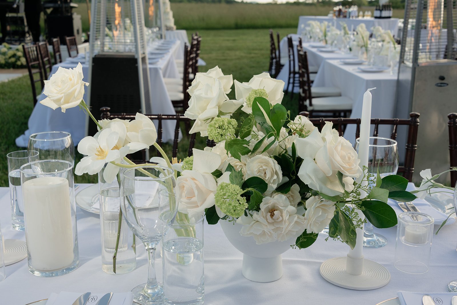 Ivory roses and white garden flowers arranged with candles along an outdoor reception table at Goodstone Inn.