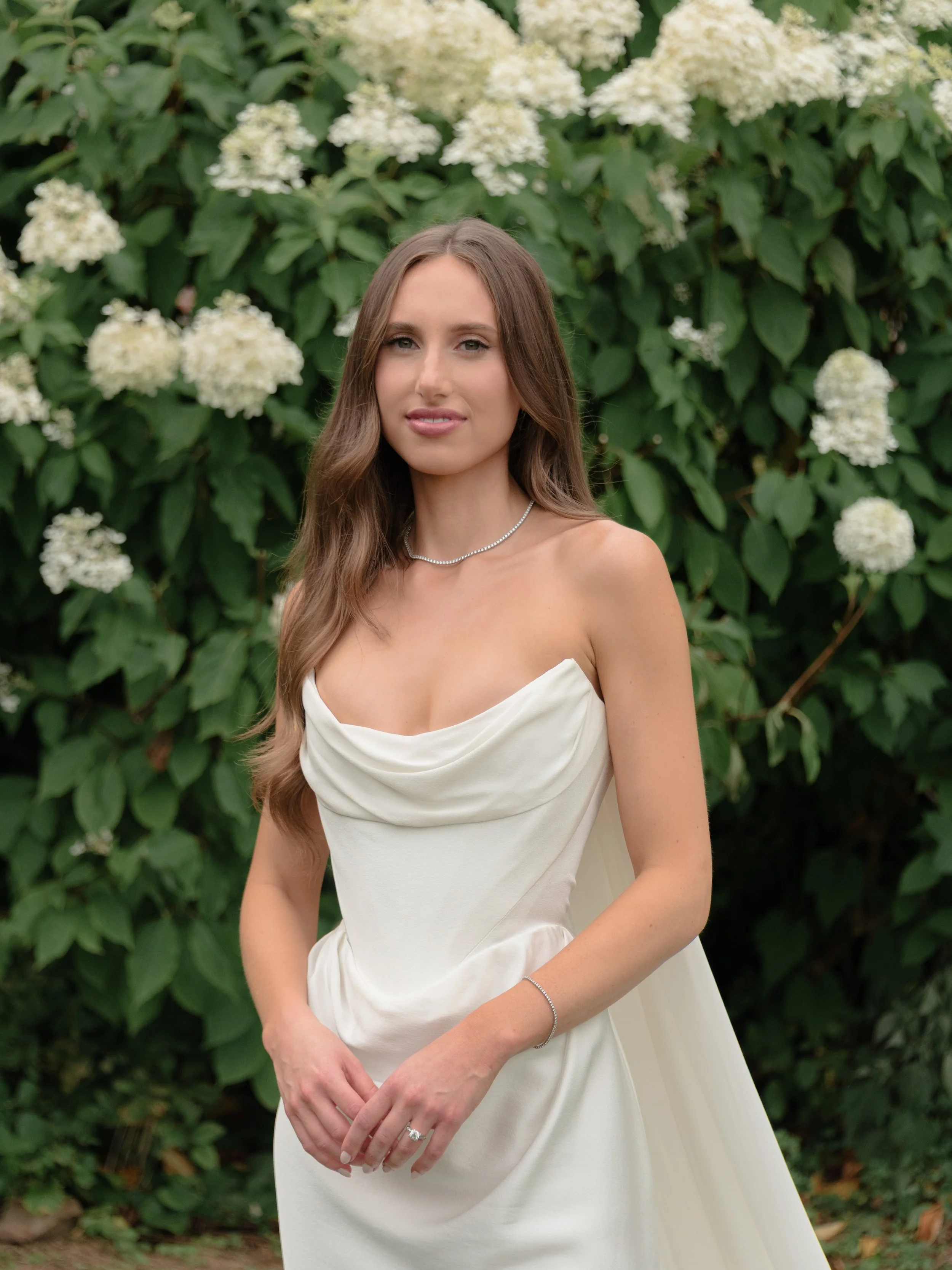 The bride wears Vivienne Westwood and the Galaxy cape as she poses in front of the blooming summer hydrangeas in front of the stone barns at Blue Hill. 
