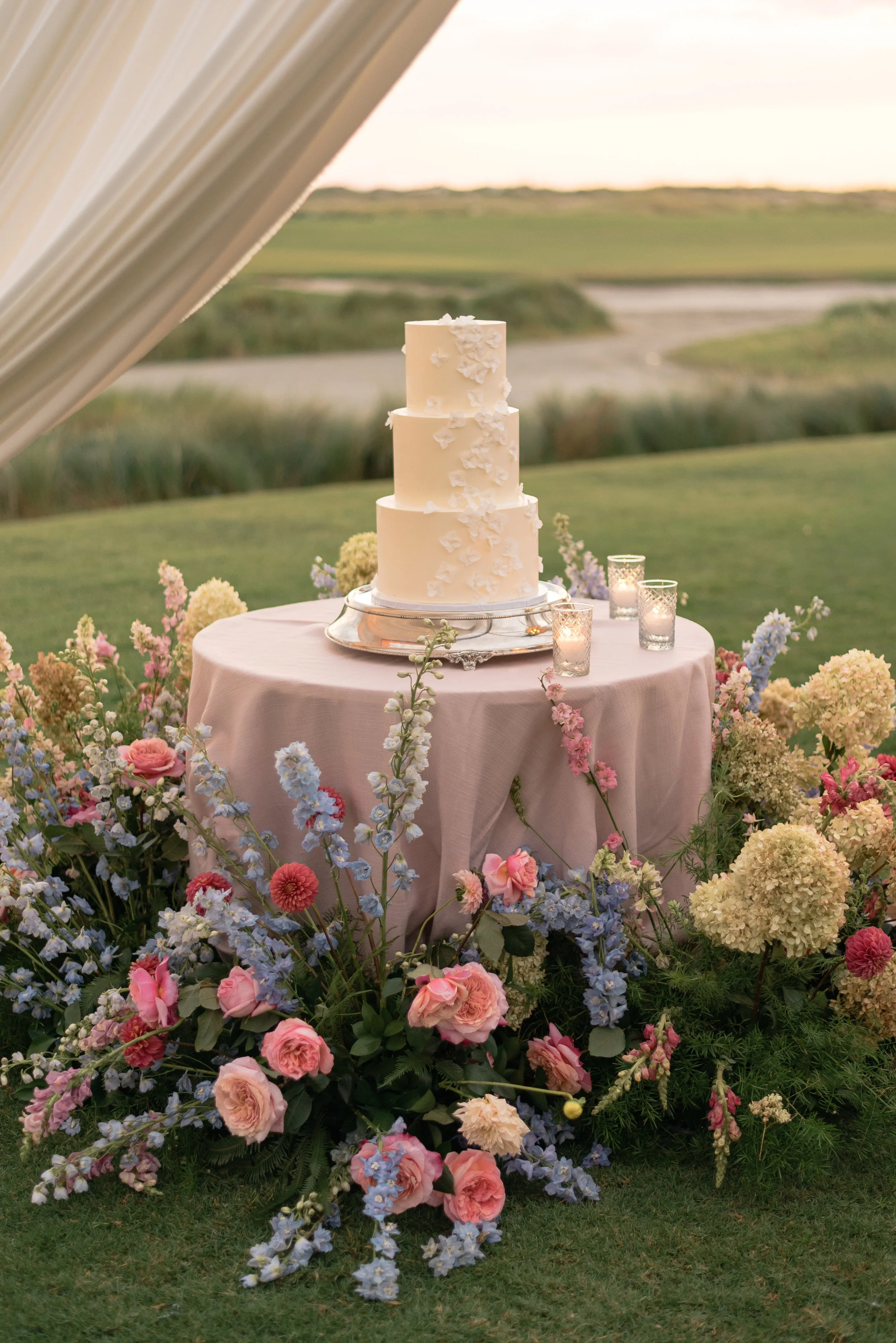 White tiered wedding cake surrounded by colorful flowers overlooks the coastal landscape at The Ocean Course.