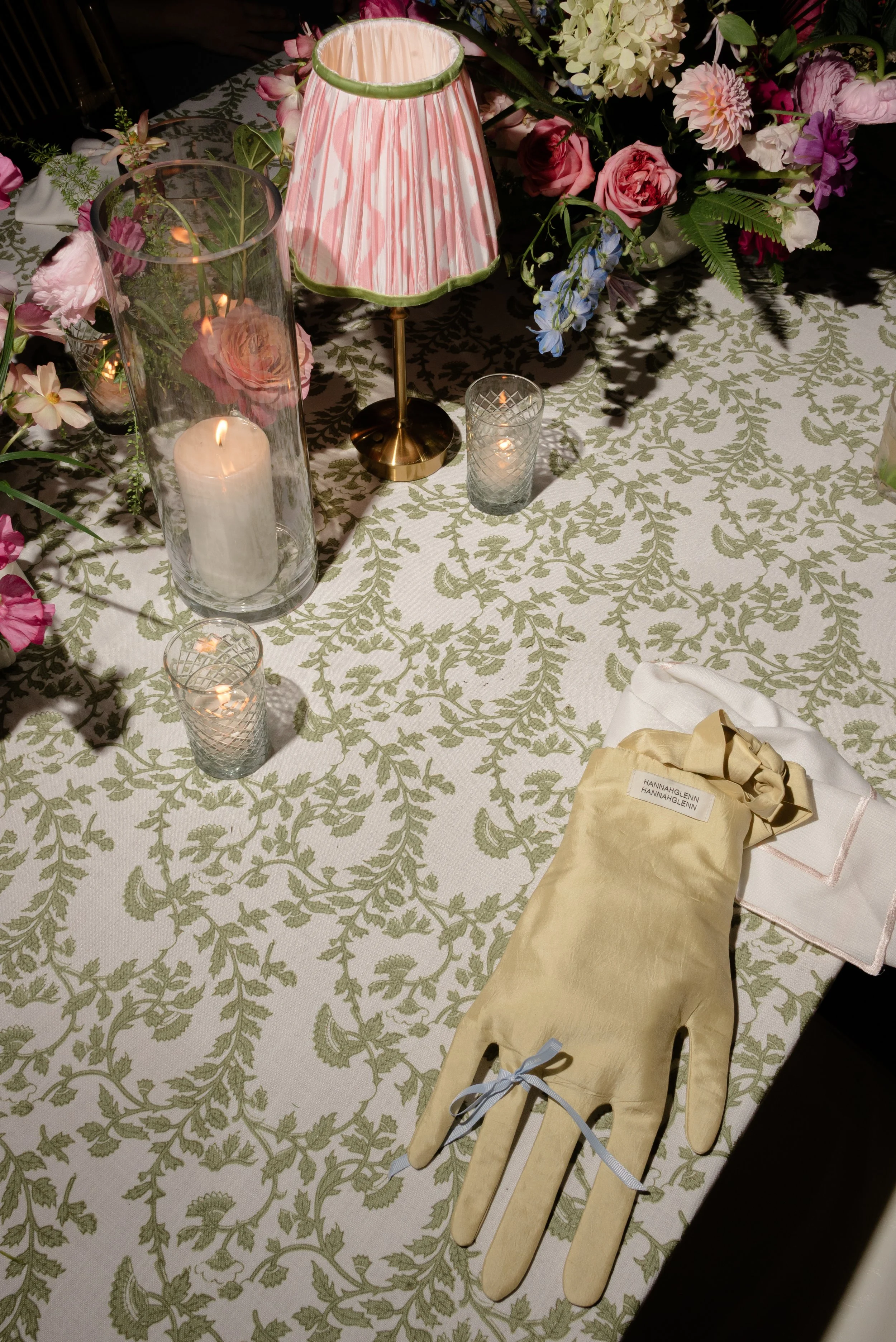 Patterned reception table with pink flowers, candlelight, a striped lamp, and a guest's glove "hand" bag.