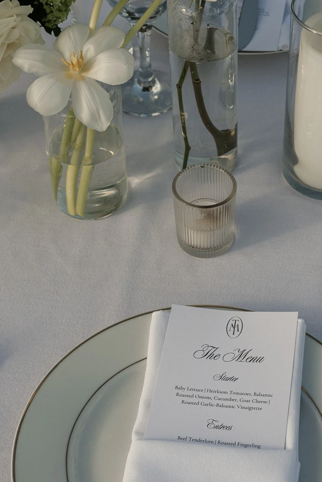 Wedding dinner menu beside clear glassware and a white flower at an outdoor Goodstone Inn reception.
