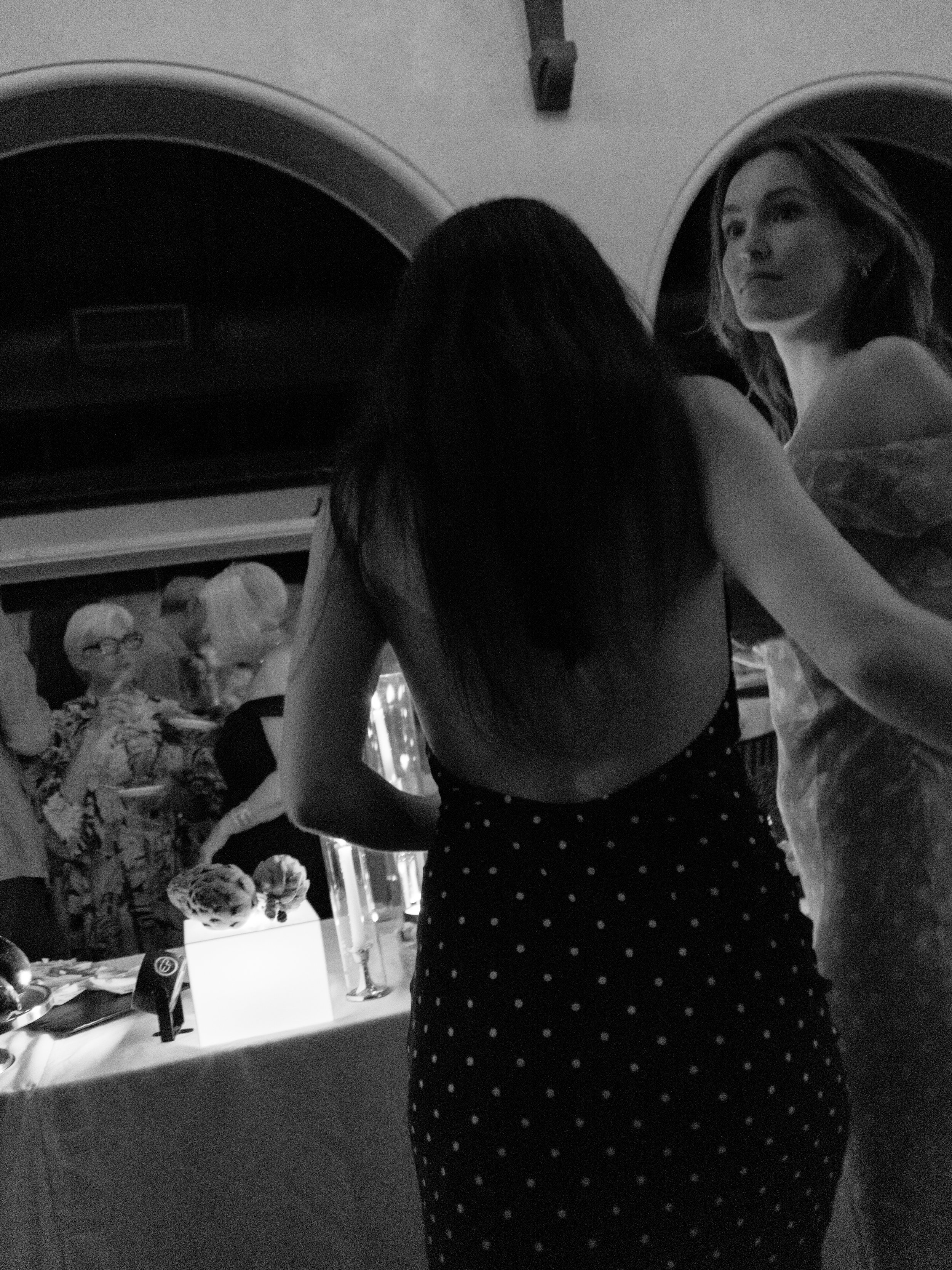 Candid photograph of two fashionable guests in polka-dot dresses gathering around the food display table like Renaissance paintings.
