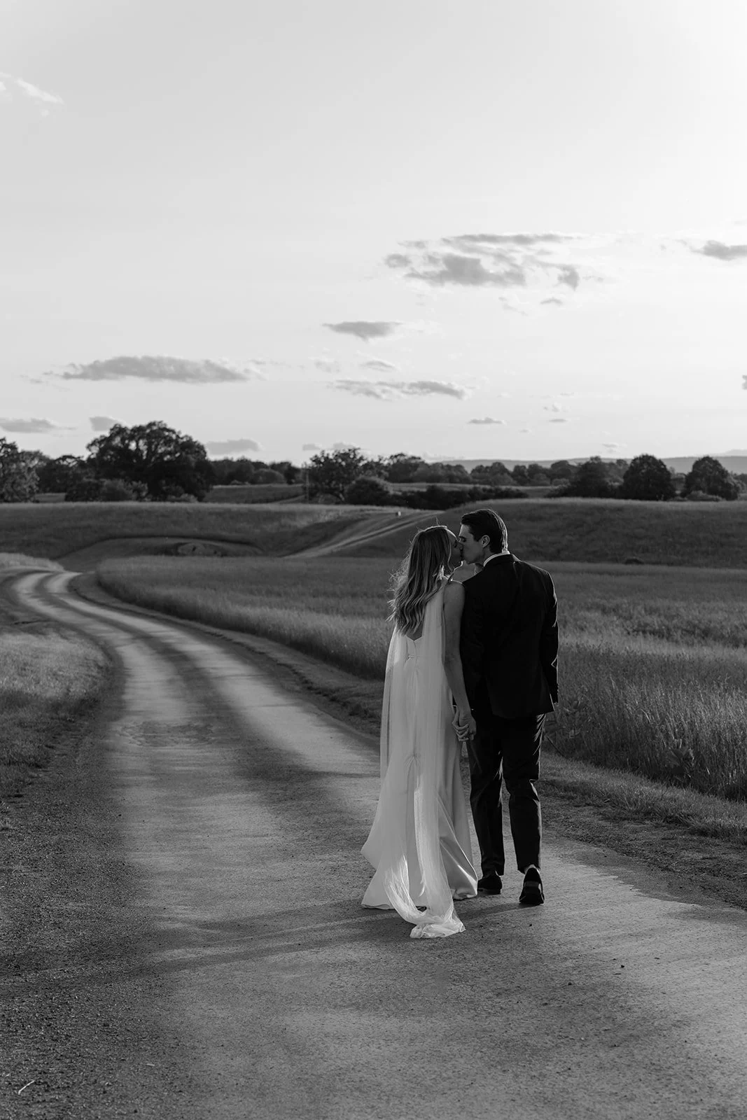 Black-and-white wide portrait of the bride and groom standing together in the open Hayfield at Goodstone Inn.