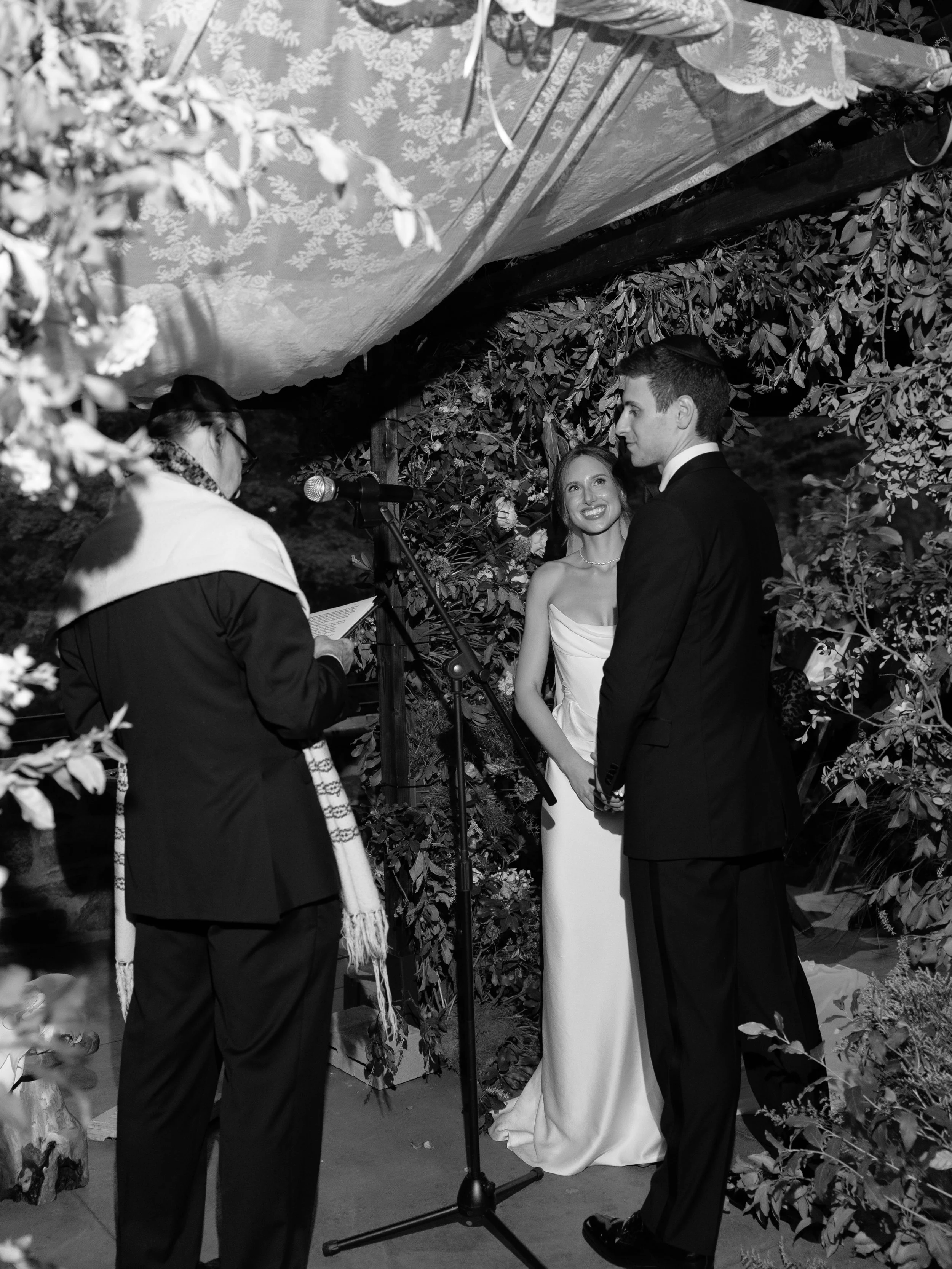 The bride beams widely at her groom beneath their chuppah during their Jewish wedding ceremony. 