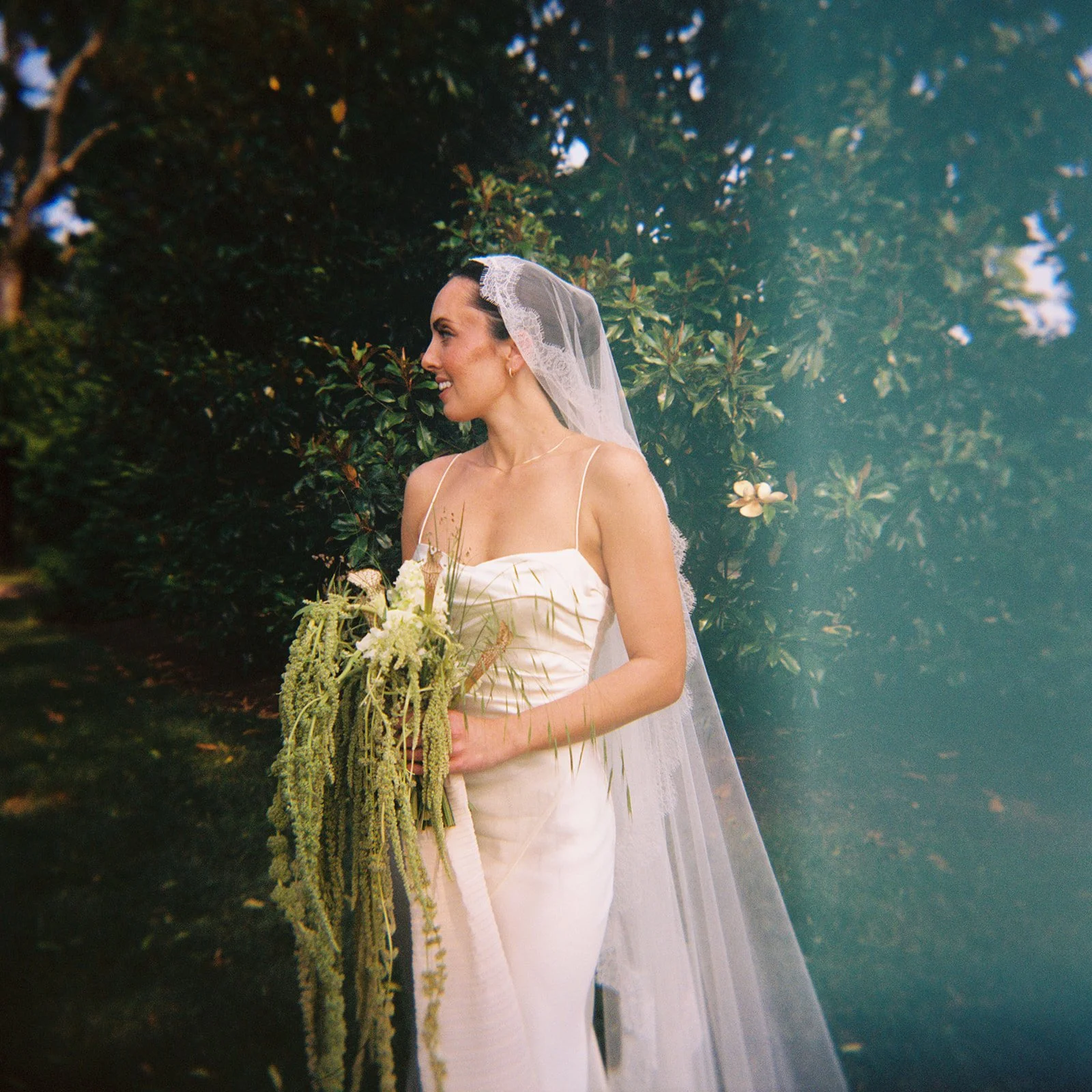 Bride wearing a lace mantilla veil and carrying a floral bouquet during a garden wedding at Ravenswood Mansion in Nashville, TN, photographed with an editorial film-inspired style.