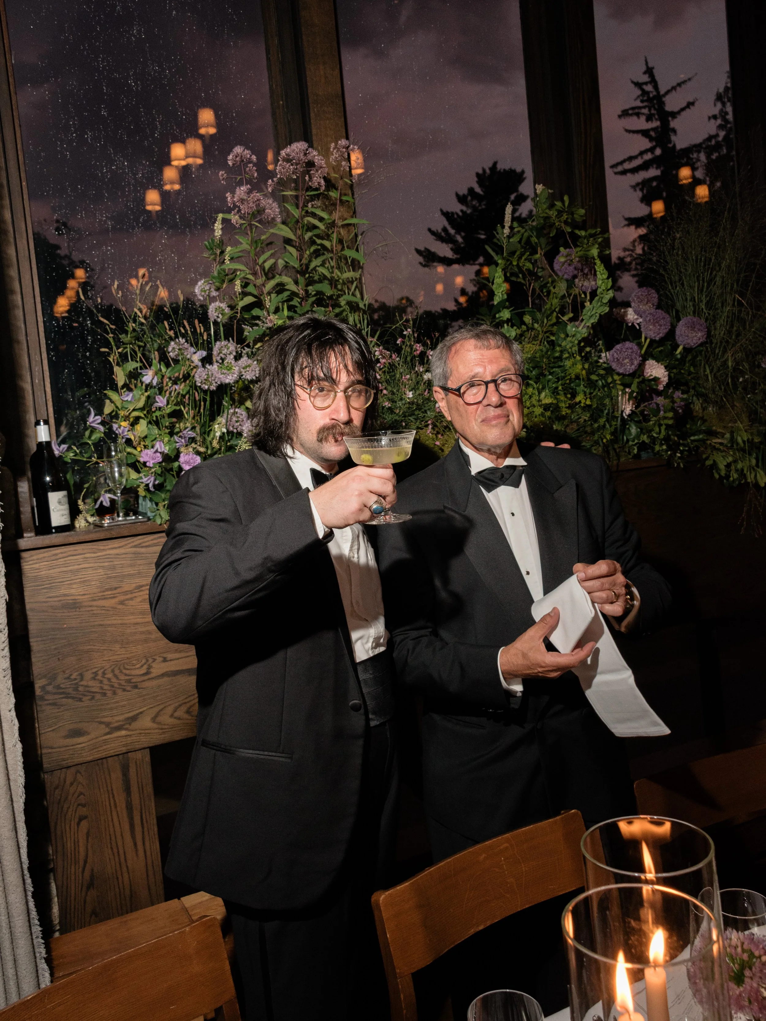 The bride's brother and father share a drink beside the floral-filled reception tables during Jennie and Will’s wedding dinner.