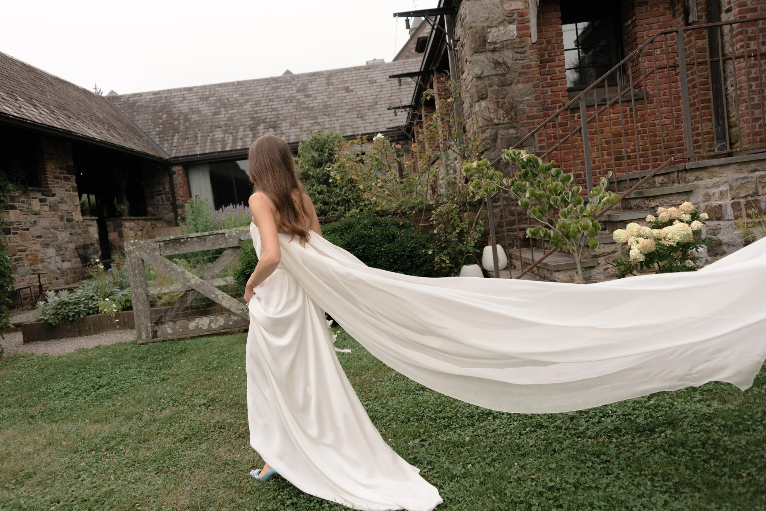 The bride's Galaxy cape flows behind her as she walks to the recognizable face of Blue Hill at Stone Barns.