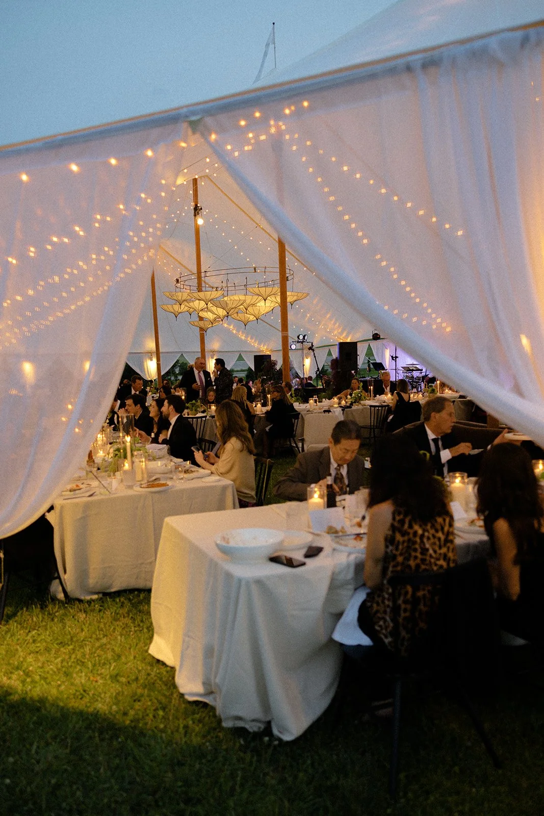 Elegant outdoor wedding reception beneath a sailcloth tent with warm lighting and intentional event design details.
