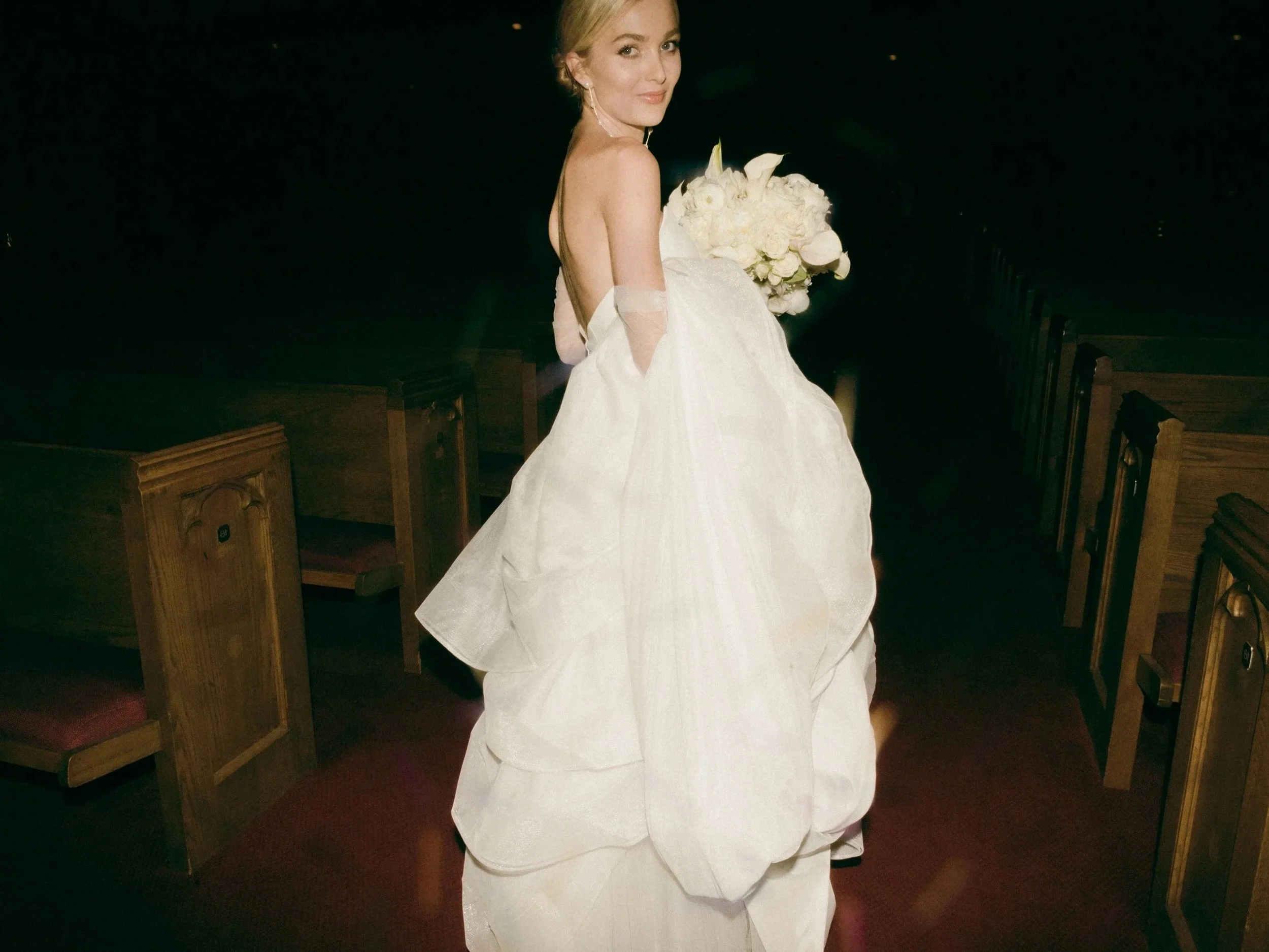 Bride in a white wedding gown holding a bouquet during an evening church wedding reception, photographed with direct flash for an editorial-inspired portrait.