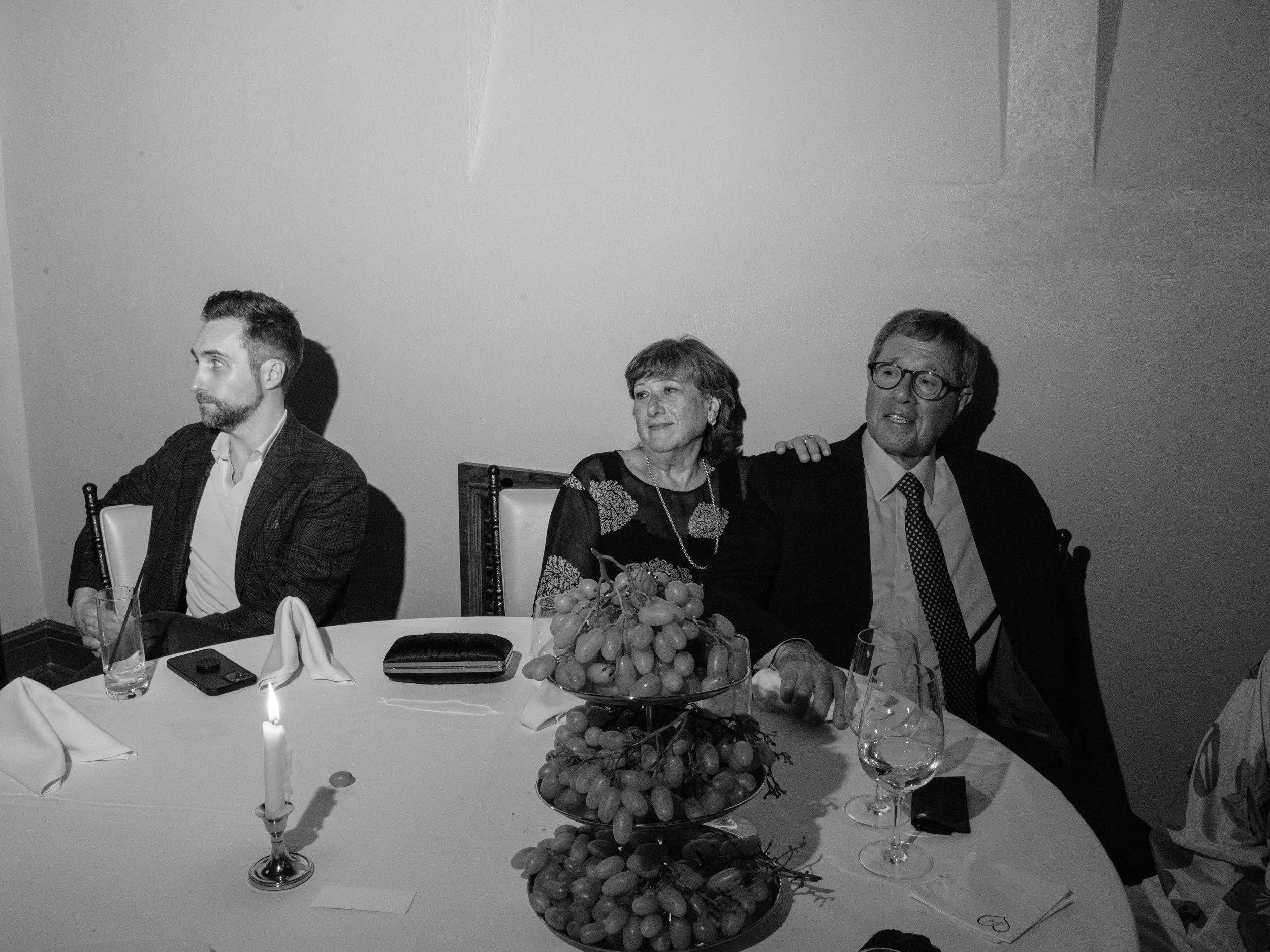 Black-and-white candid of family members seated together listening during rehearsal dinner speeches.