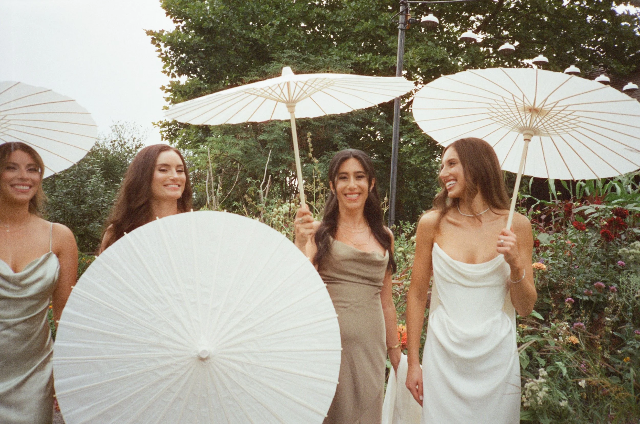 A film photo of Jennie and her bridesmaids posing with white parasols among the summer gardens at Blue Hill at Stone Barns.