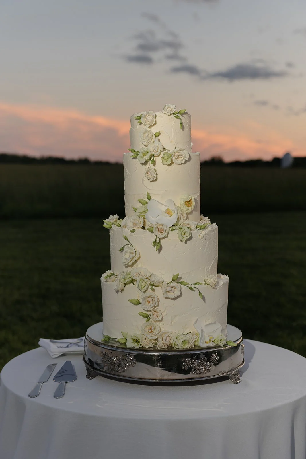 White tiered wedding cake with delicate floral details displayed outdoors at sunset at Goodstone Inn.