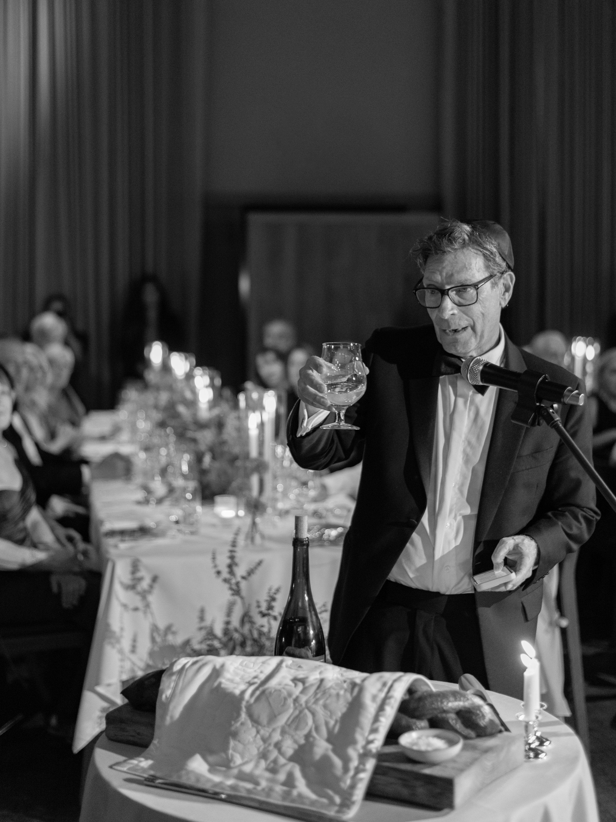 Black-and-white portrait of the groom's father giving a wedding speech during dinner.