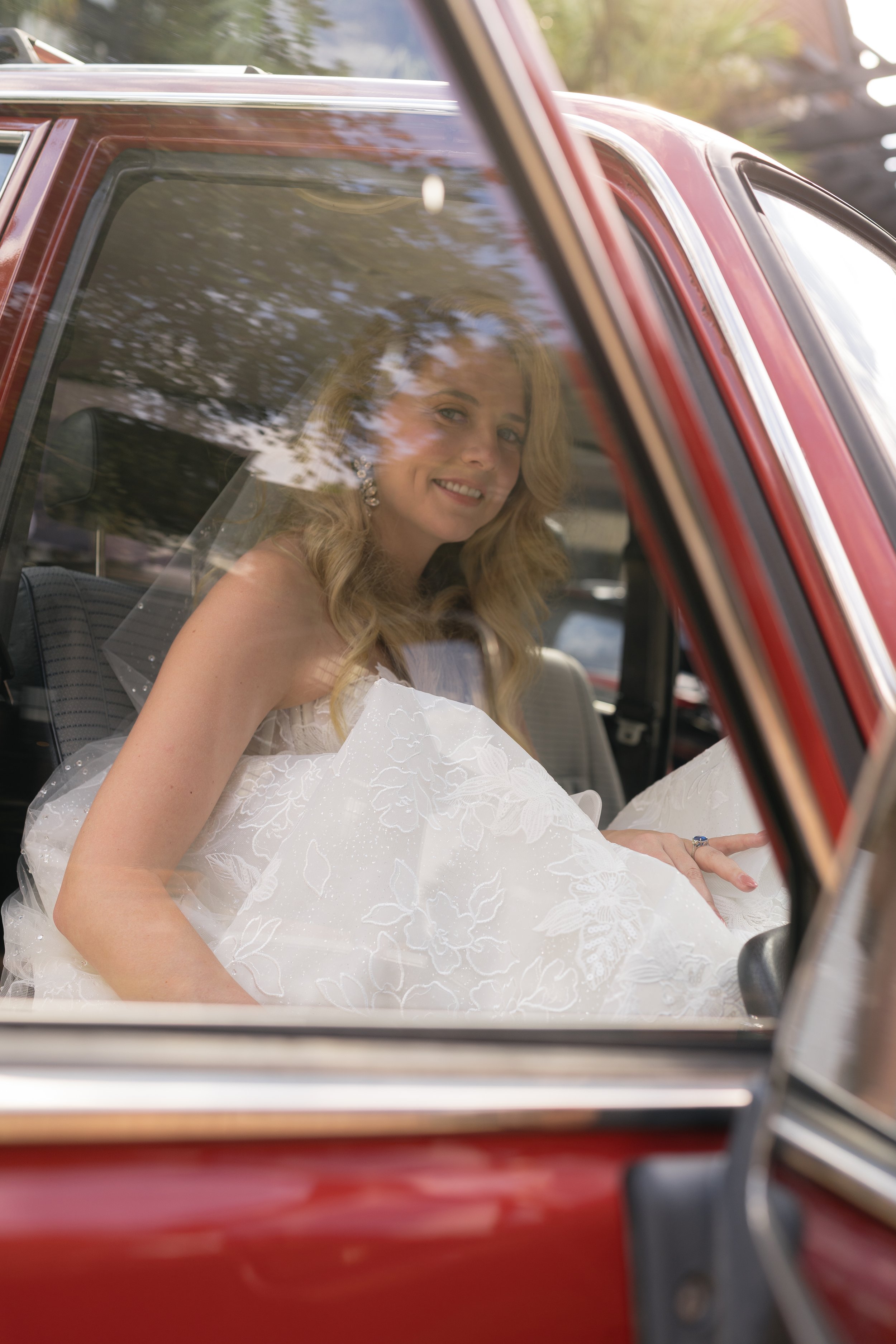 Katie smiles from the passenger seat of a vintage red Bronco as she leaves the private estate for her Ocean Course ceremony.