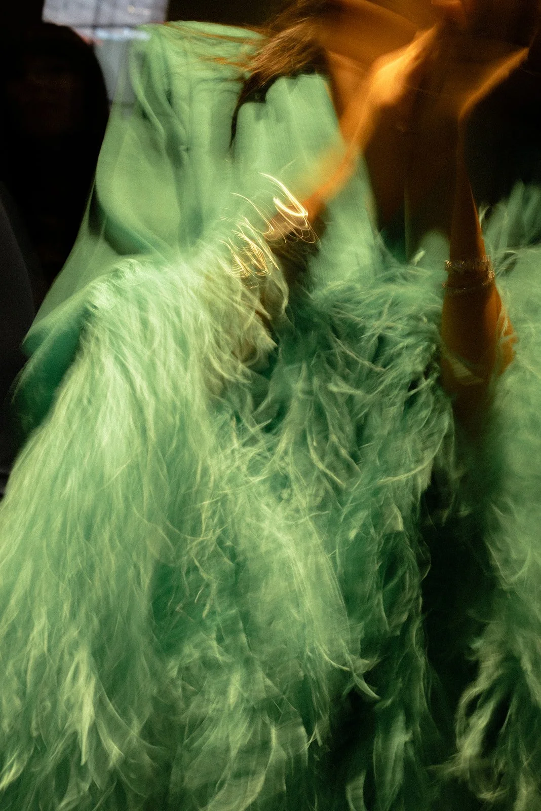 Abstract editorial photograph of a guest’s textured green feather garment during an evening celebration, capturing fashion, movement, and expressive personal style.