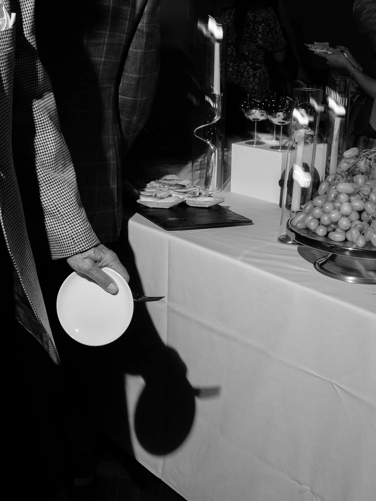 Black and white editorial photograph of a hospitality detail during an event, capturing food, service, and the intimate moments surrounding a gathering.