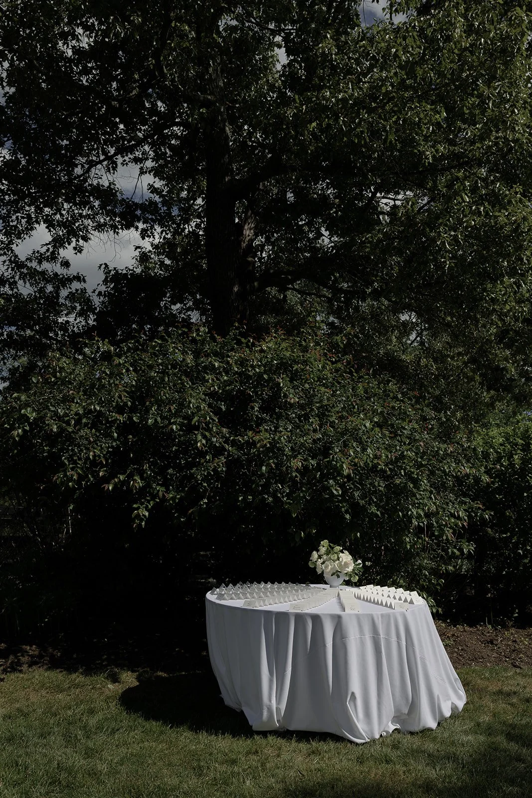 White linen-covered wedding display table positioned outdoors beneath mature trees at Goodstone Inn.