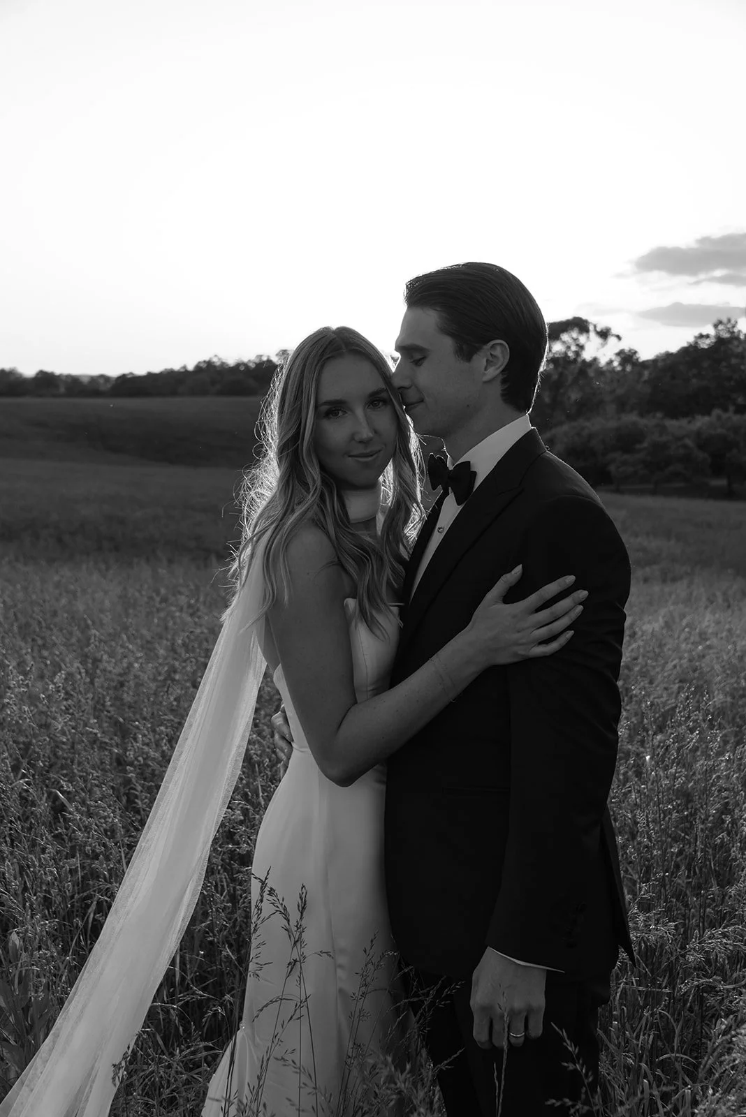 Bride and groom embracing closely during sunset portraits in the field at Goodstone Inn.
