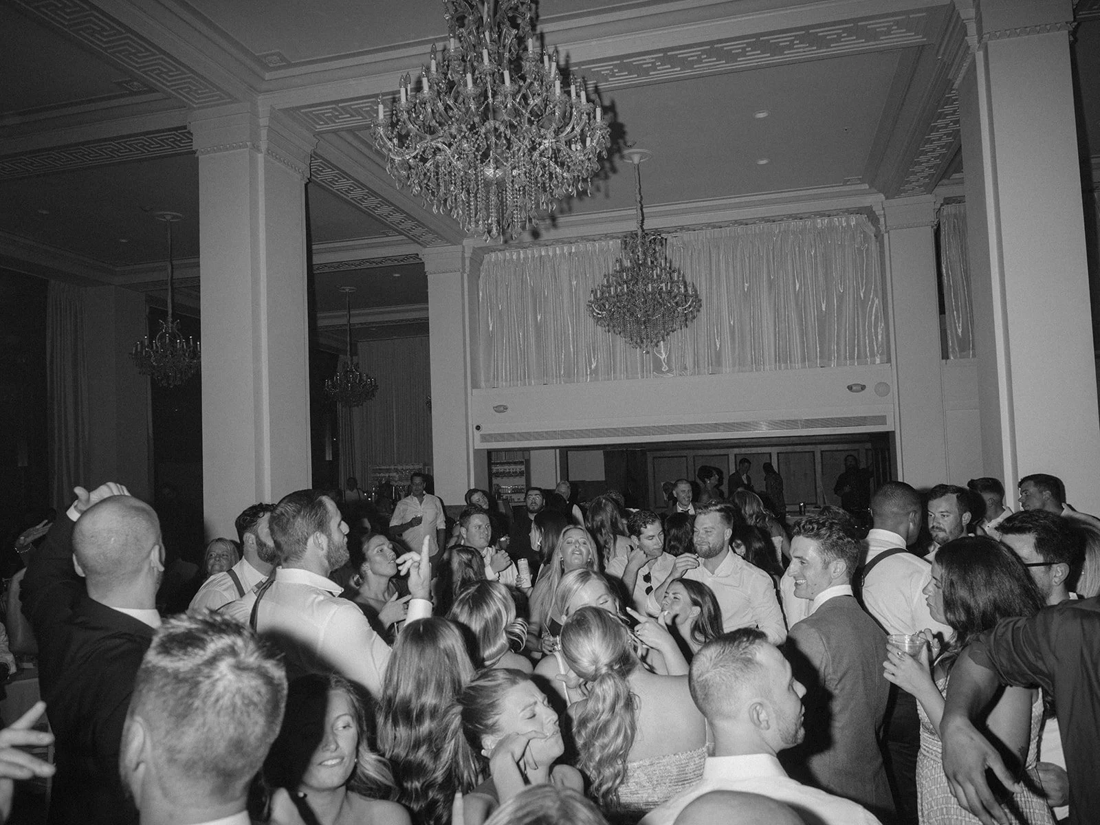 Black-and-white documentary photograph of a crowded wedding reception beneath chandeliers in a classic ballroom in Providence, Rhode Island.