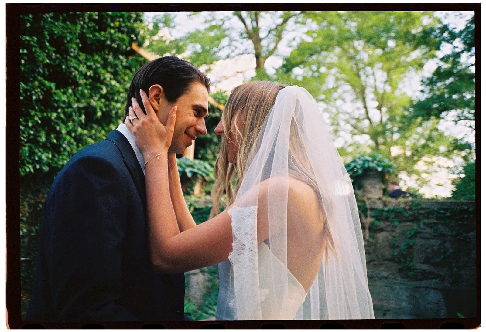 Bride and groom embracing beneath her veil in the lush gardens at Goodstone Inn.