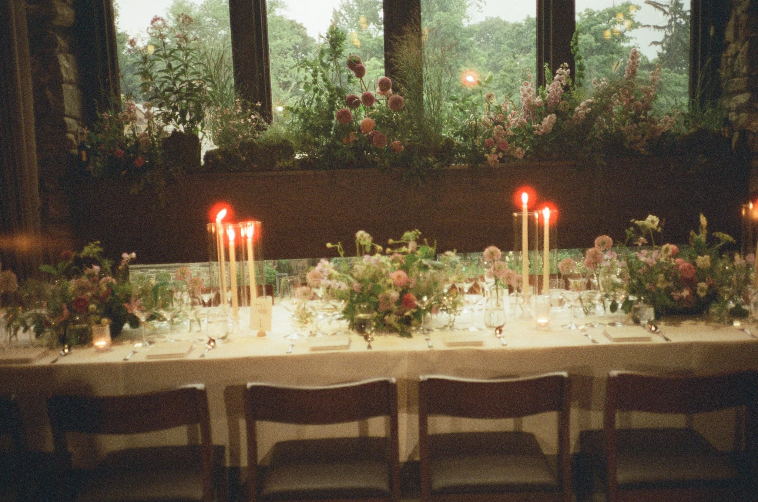 Film photograph of a long reception table layered with summer flowers and glowing red taper candles at Blue Hill at Stone Barns.