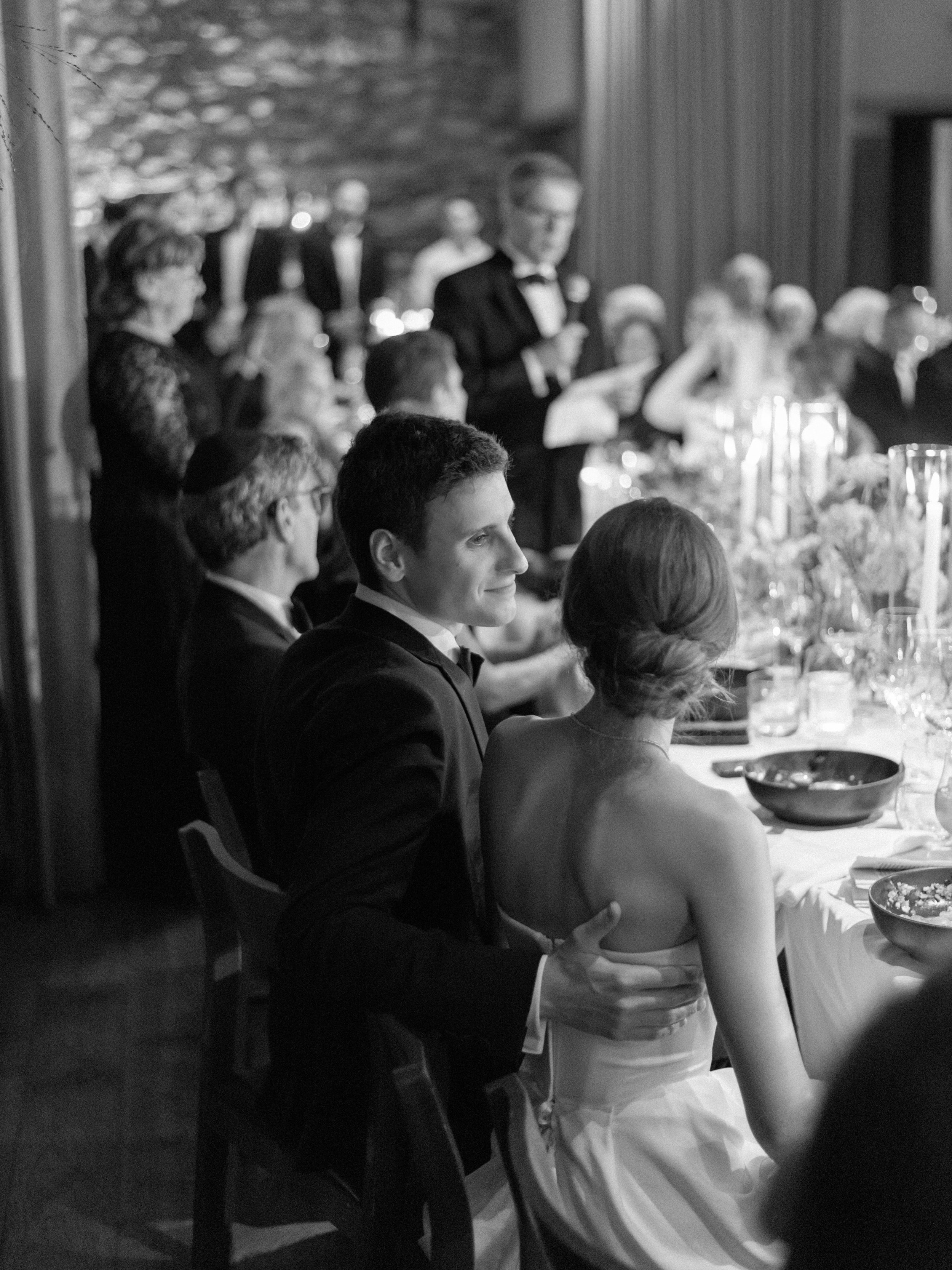 Black-and-white candid of Will looking at Jennie seated at dinner among candlelight and family conversation.