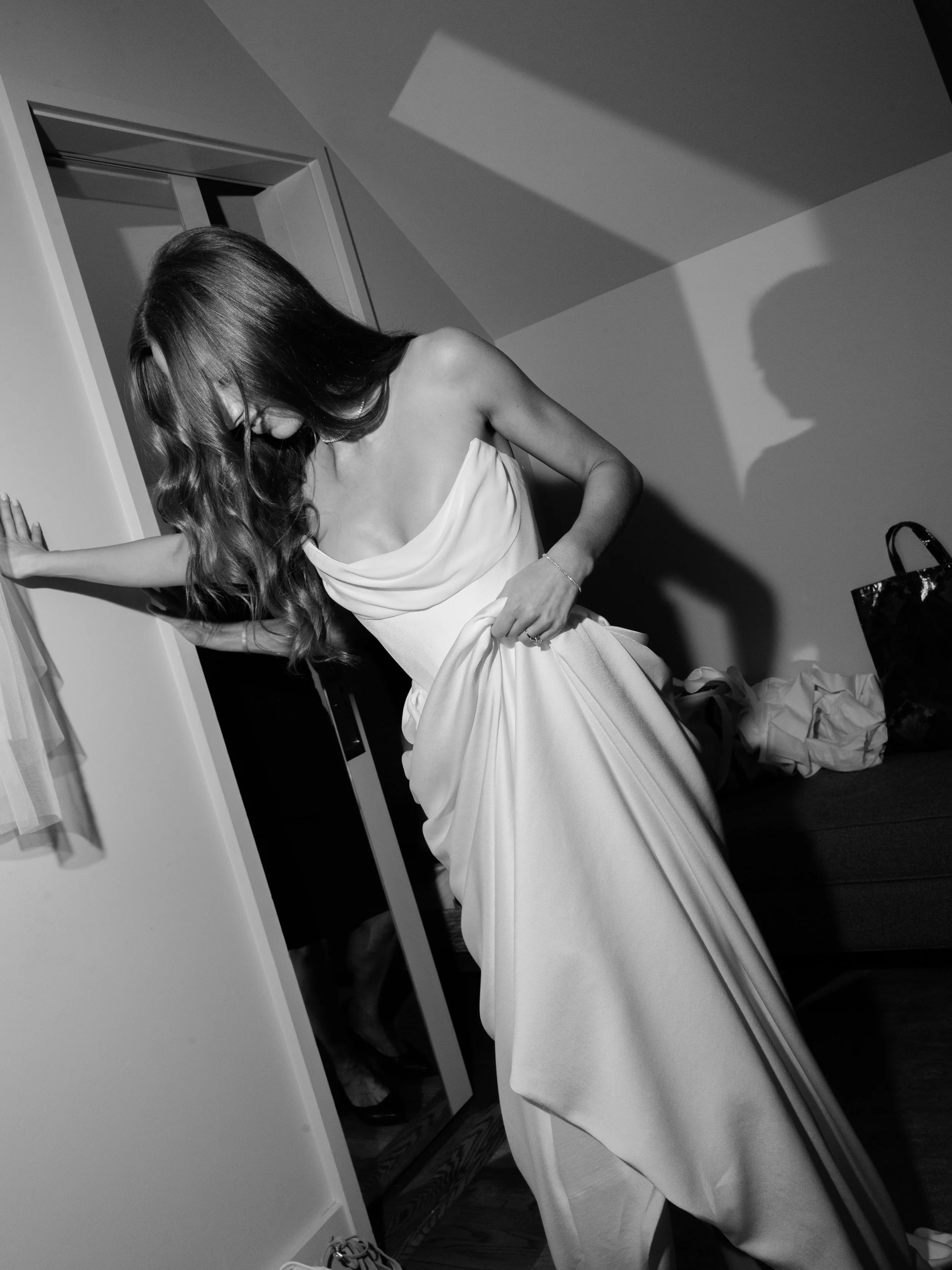 Black and white editorial photograph of a bride adjusting her wedding dress in a quiet moment before the ceremony.