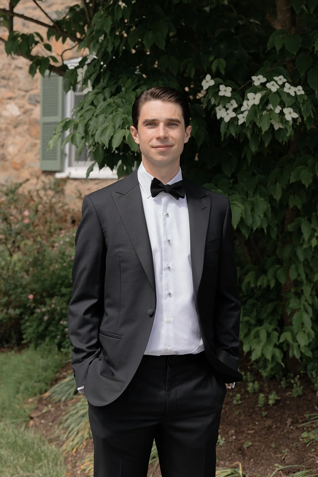 Groom standing outdoors at Goodstone Inn surrounded by lush spring greenery.