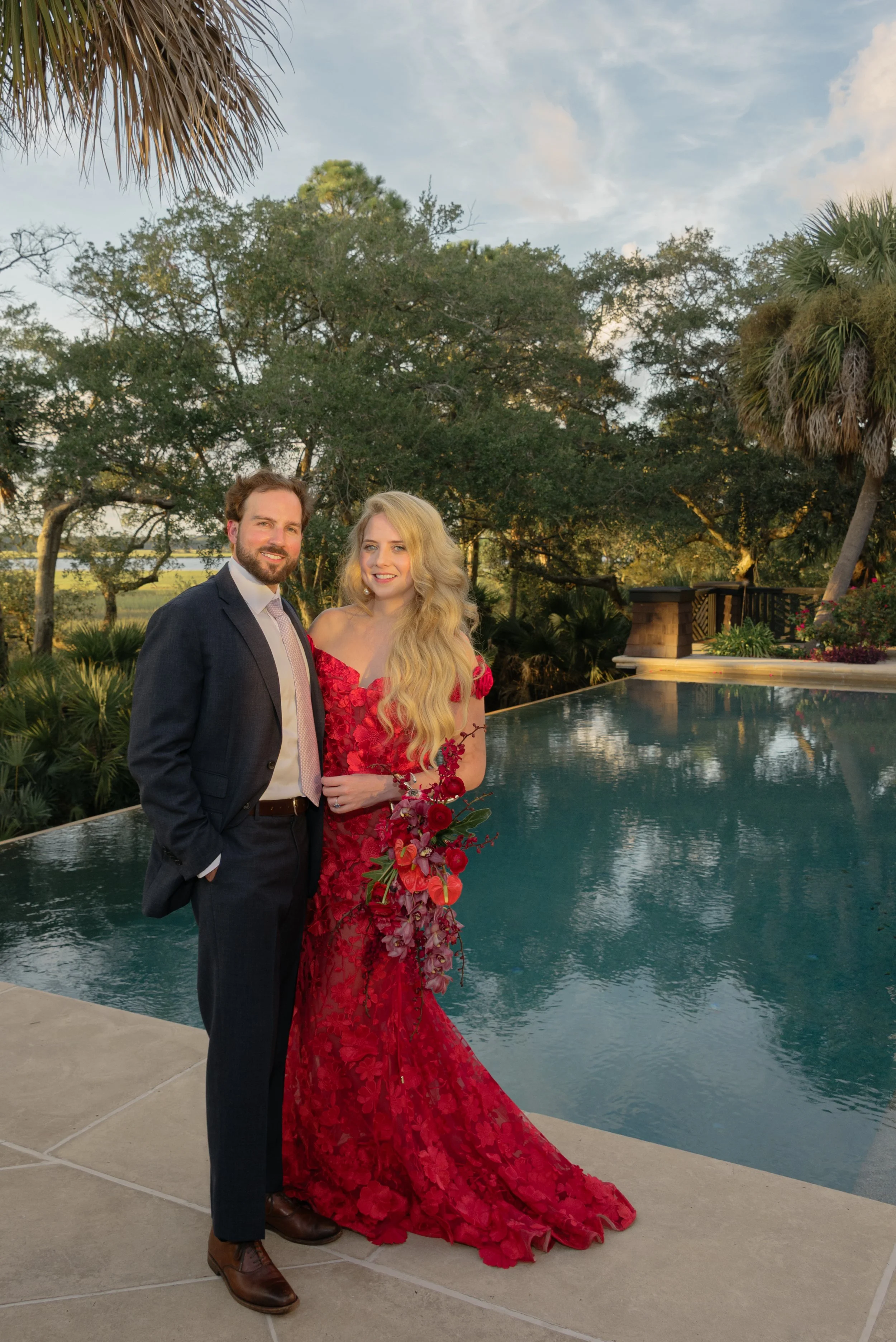 Katie and Trevor pose beside the pool before their Kiawah Island rehearsal dinner, with Katie wearing a red Bronx and Banco Jasmine gown.