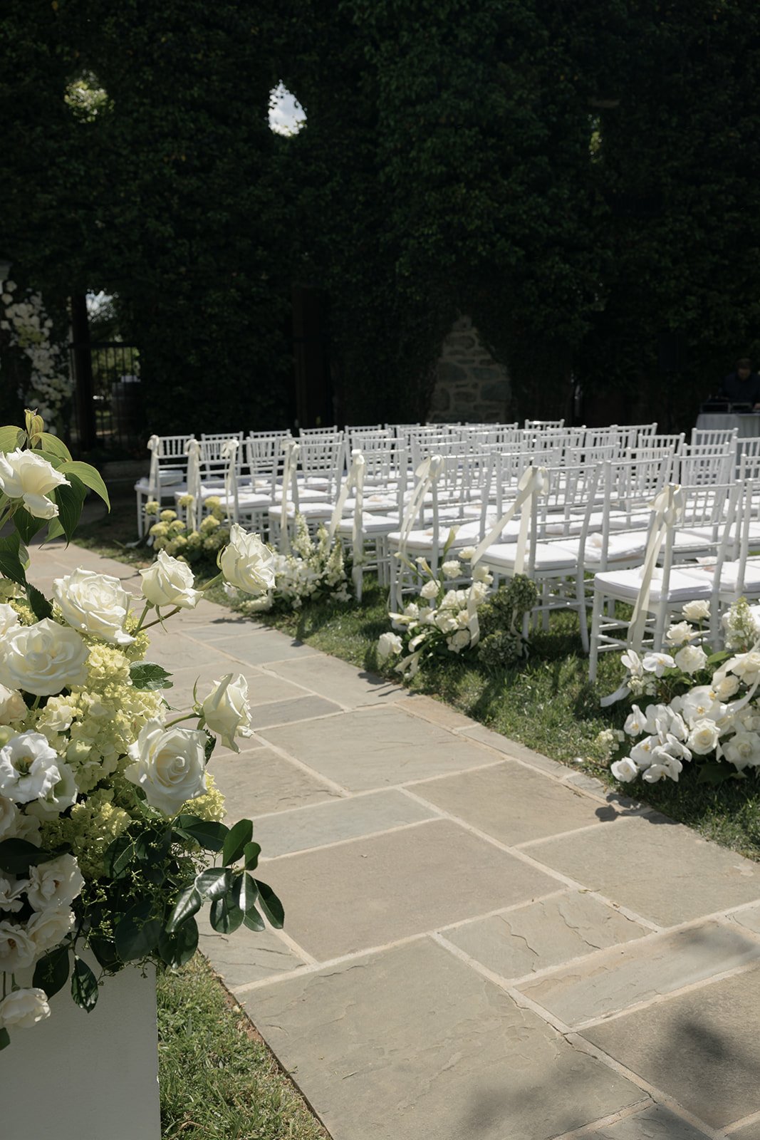 White floral arrangements designed by Steelcut Flower Co. lining the stone ceremony aisle at Goodstone Inn against deep green ivy.