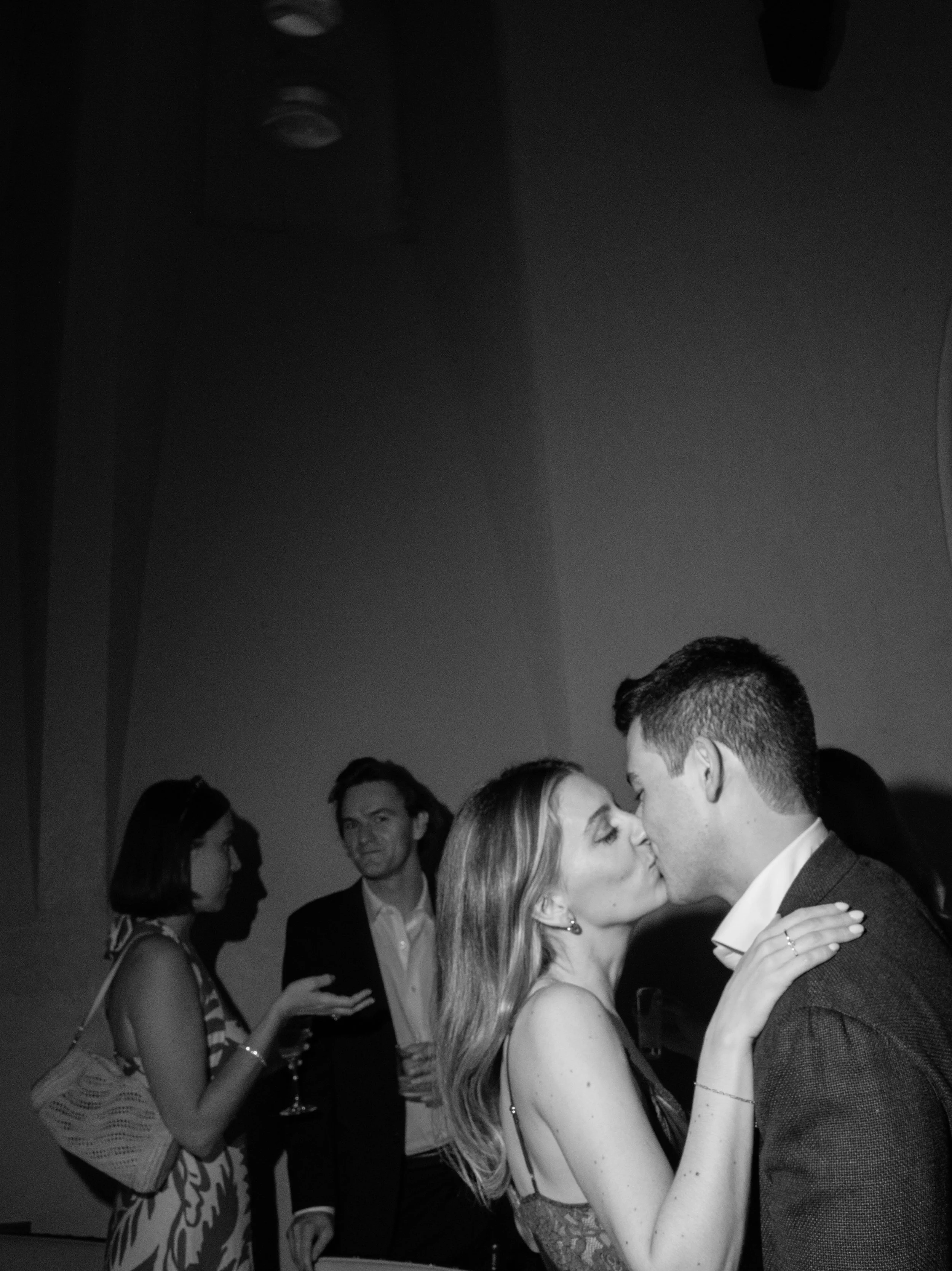 Black-and-white candid of a couple kissing during the intimate rehearsal dinner celebration.