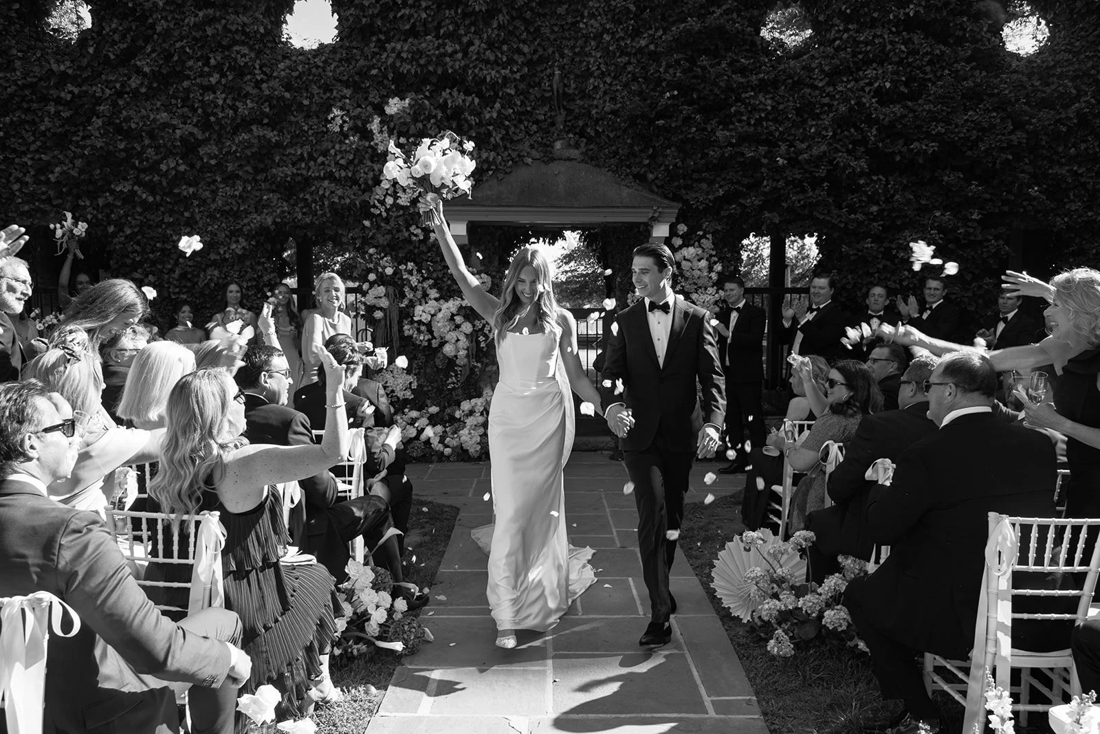 Black-and-white photograph of wedding guests celebrating as the newlyweds walk back up the aisle at Goodstone Inn.
