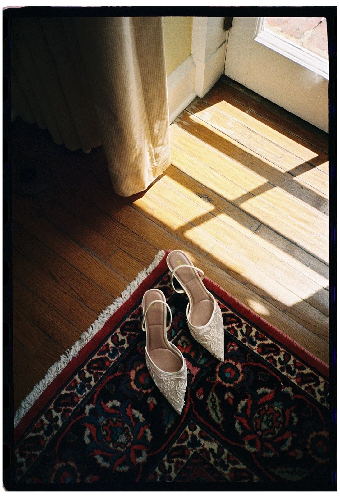 Film photo of bridal shoes resting on a patterned rug beside warm window light at Goodstone Inn.