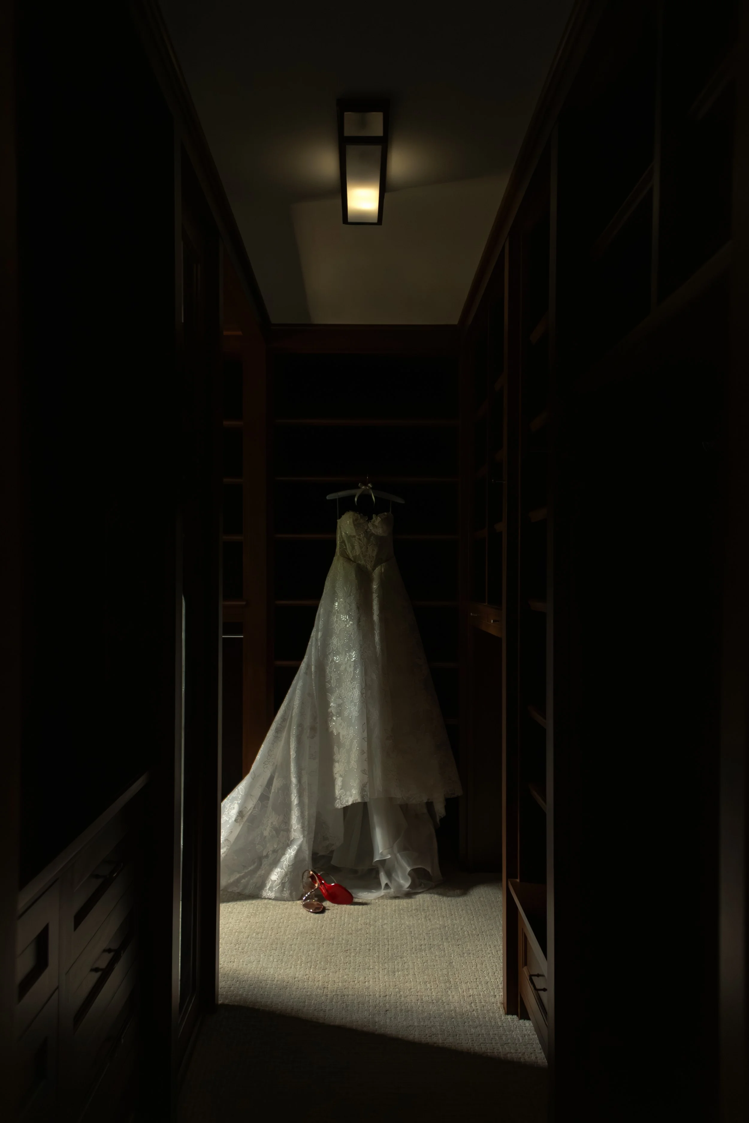 Katie’s Galia Lahav wedding gown hangs in a dark wood-paneled corridor above her red-soled Christian Louboutin heels.