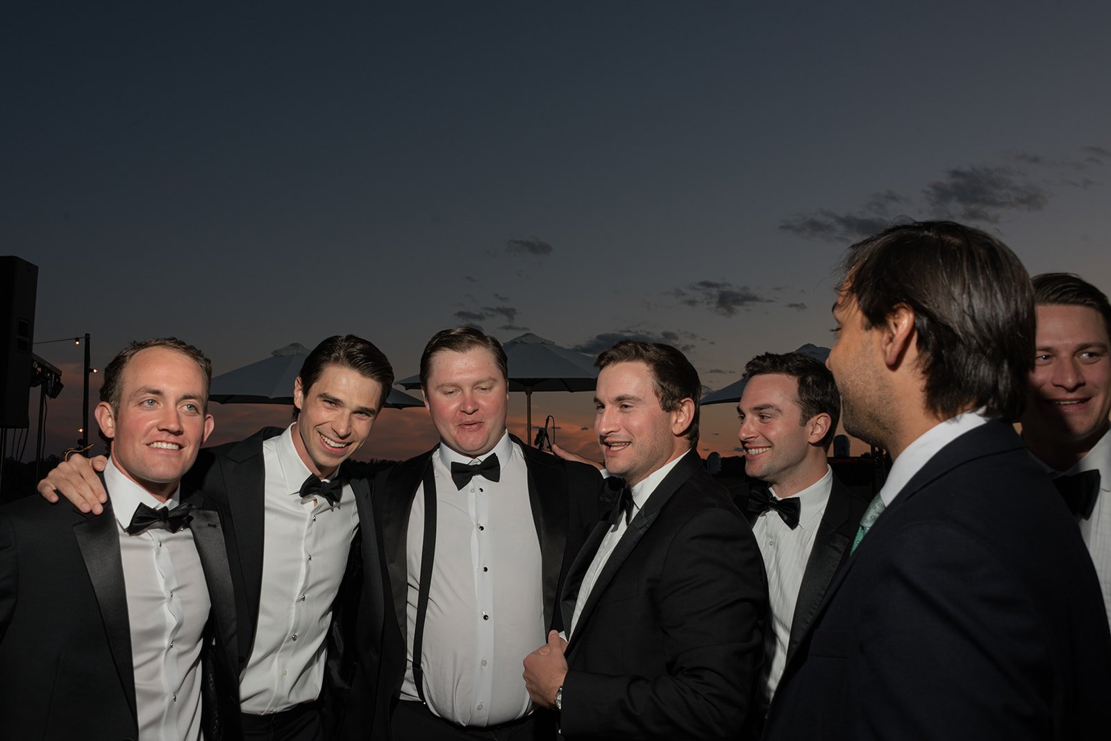Groom and groomsmen gathered together in black tuxedos beneath an evening sky at Goodstone Inn.