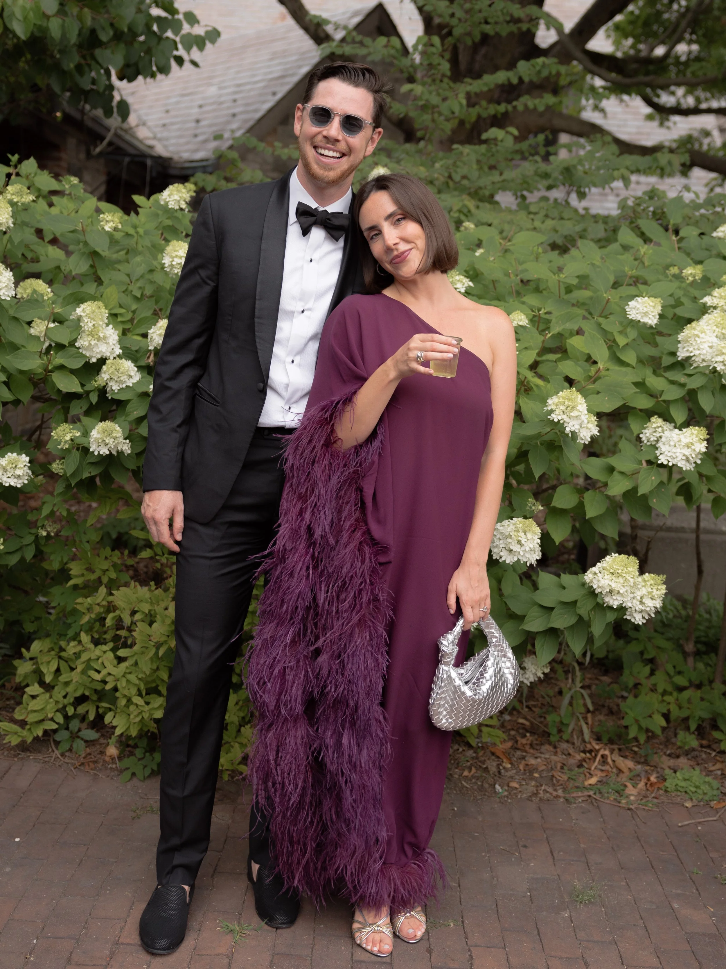 Fabulous guests arrive in black-tie and wearing a cold-shoulder eggplant purple maxi-dress with ostrich feathers and a Swarovski clutch. 