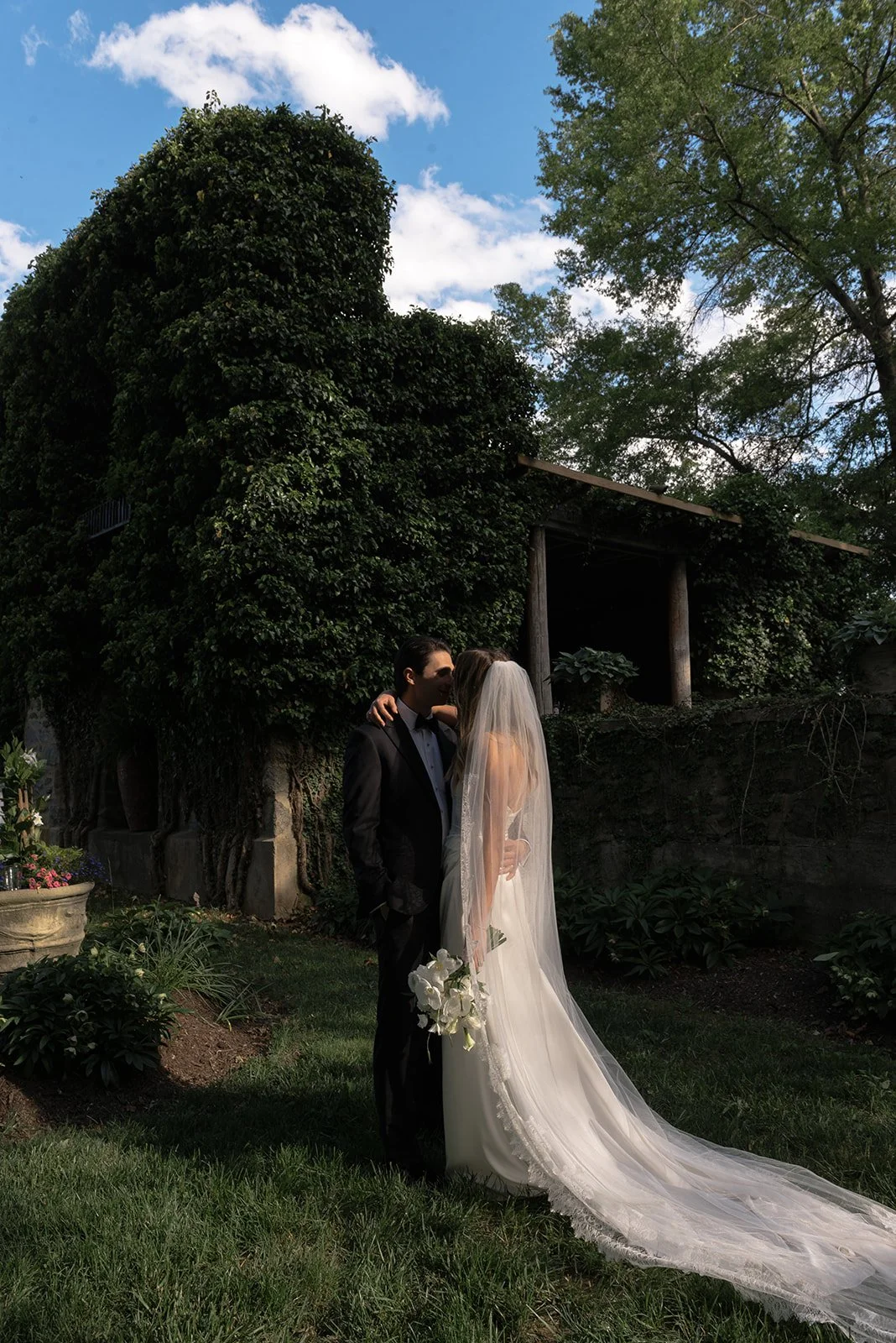 Bride and groom kissing in the gardens at Goodstone Inn with the bride’s long cathedral veil trailing across the grass.