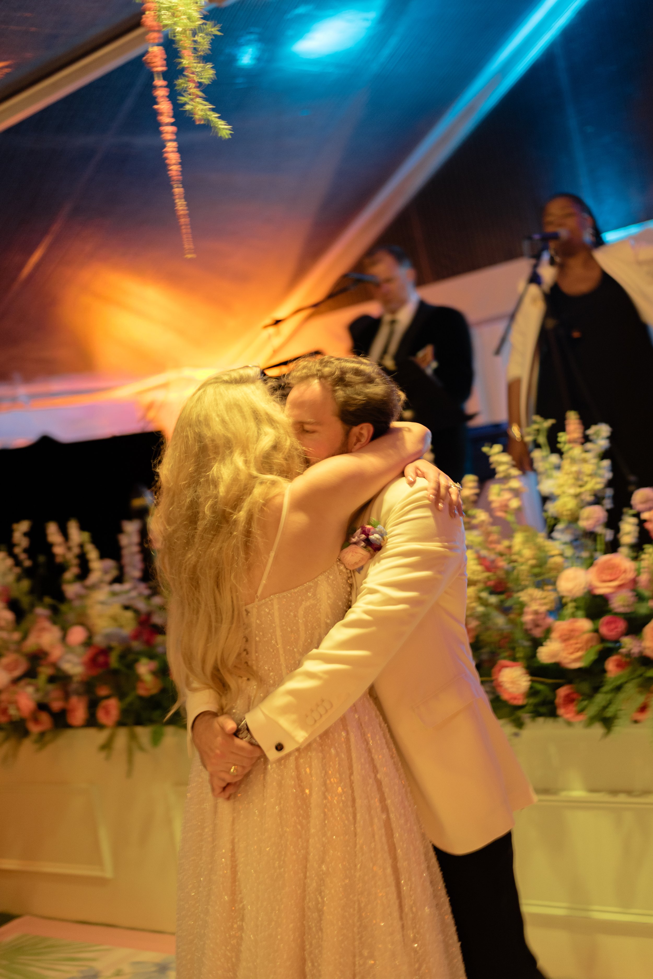 Katie and Trevor embrace and kiss inside their flower-filled wedding reception tent.