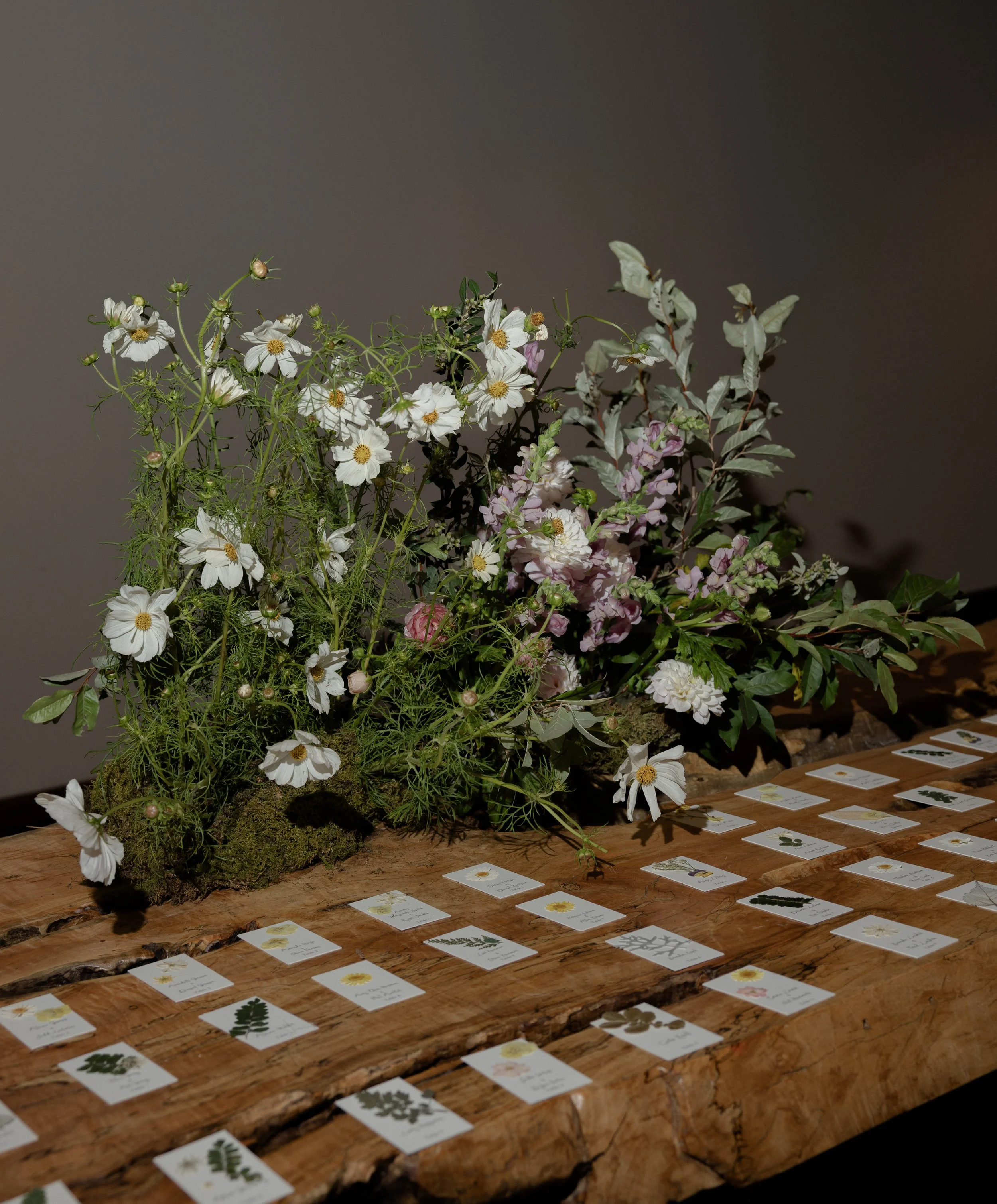 Garden-inspired escort-card installation combining handwritten botanical place cards with abundant seasonal flowers designed by Mudari Creative.