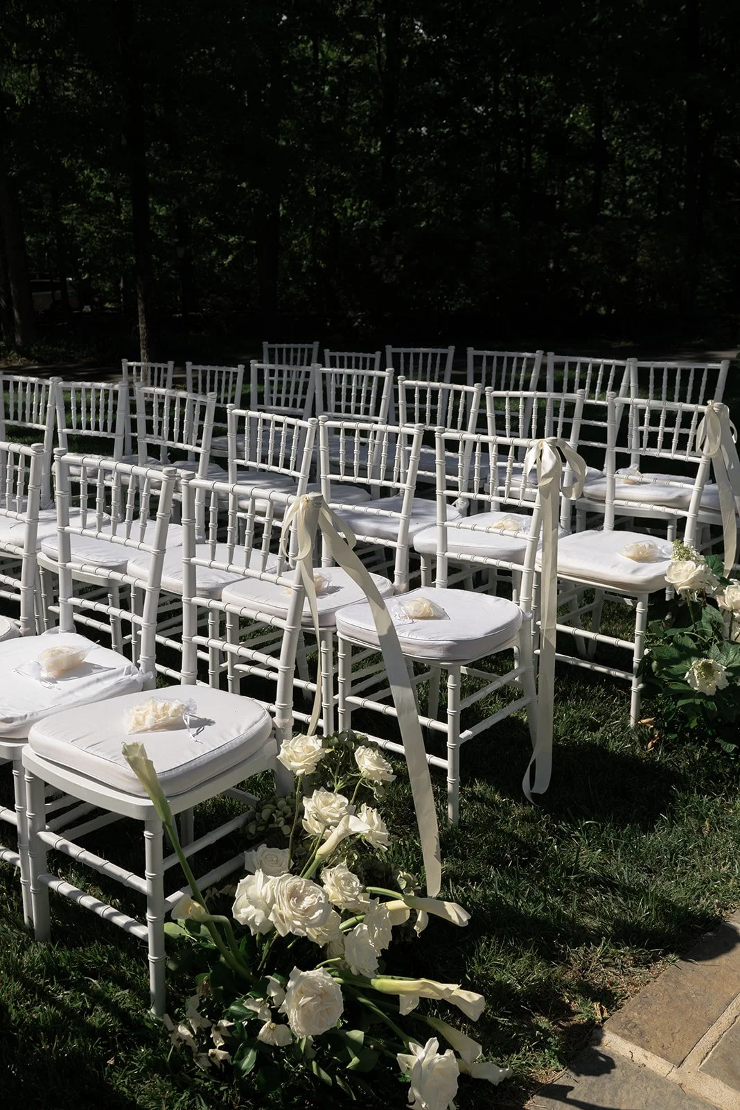 White ceremony chairs decorated with ivory flowers along a garden aisle at Goodstone Inn.