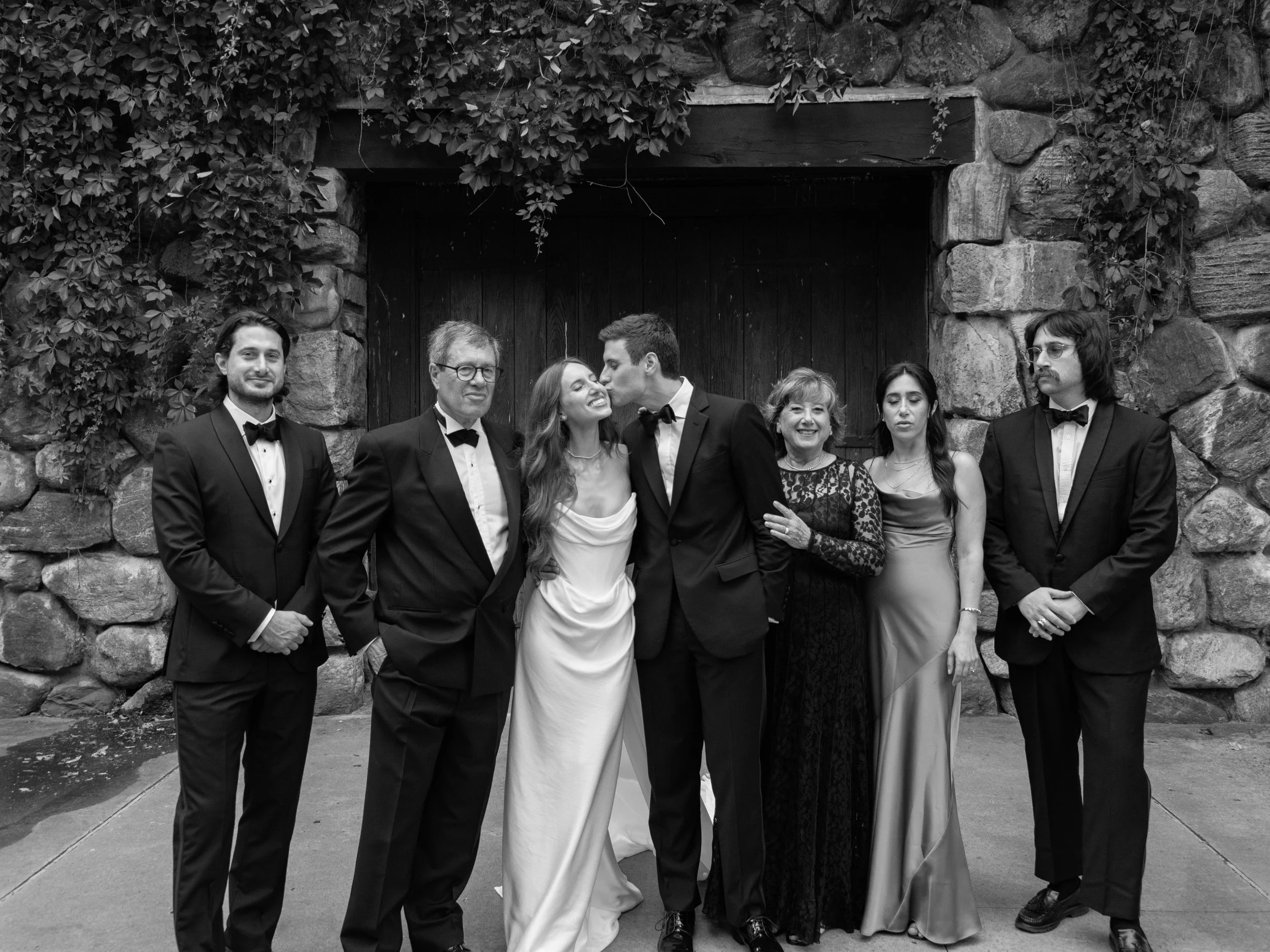 Black-and-white extended family portrait with Jennie and Will outside the historic stone buildings at Blue Hill at Stone Barns.