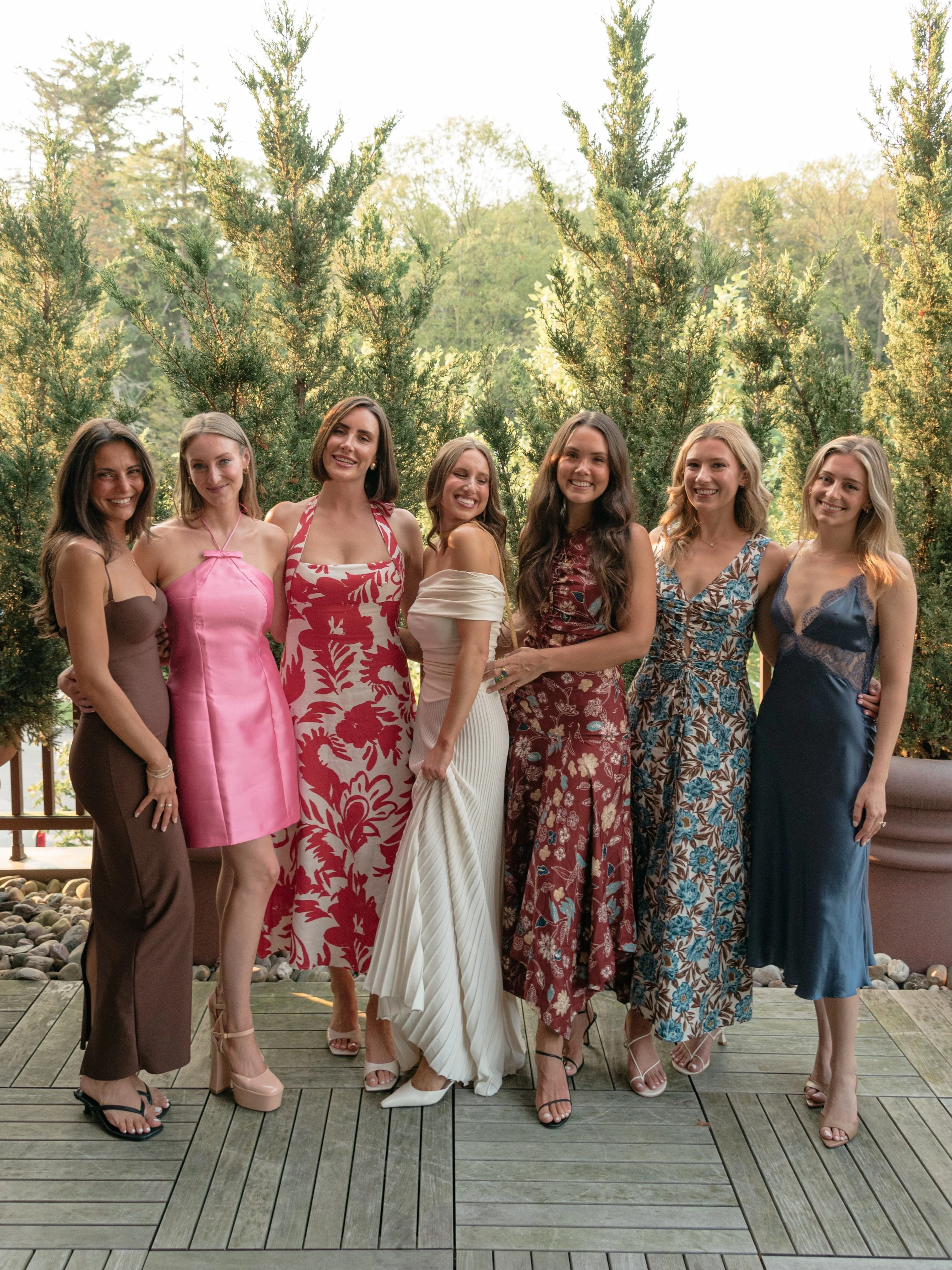Bride poses with a group of women in colorful summer dresses before the rehearsal dinner.
