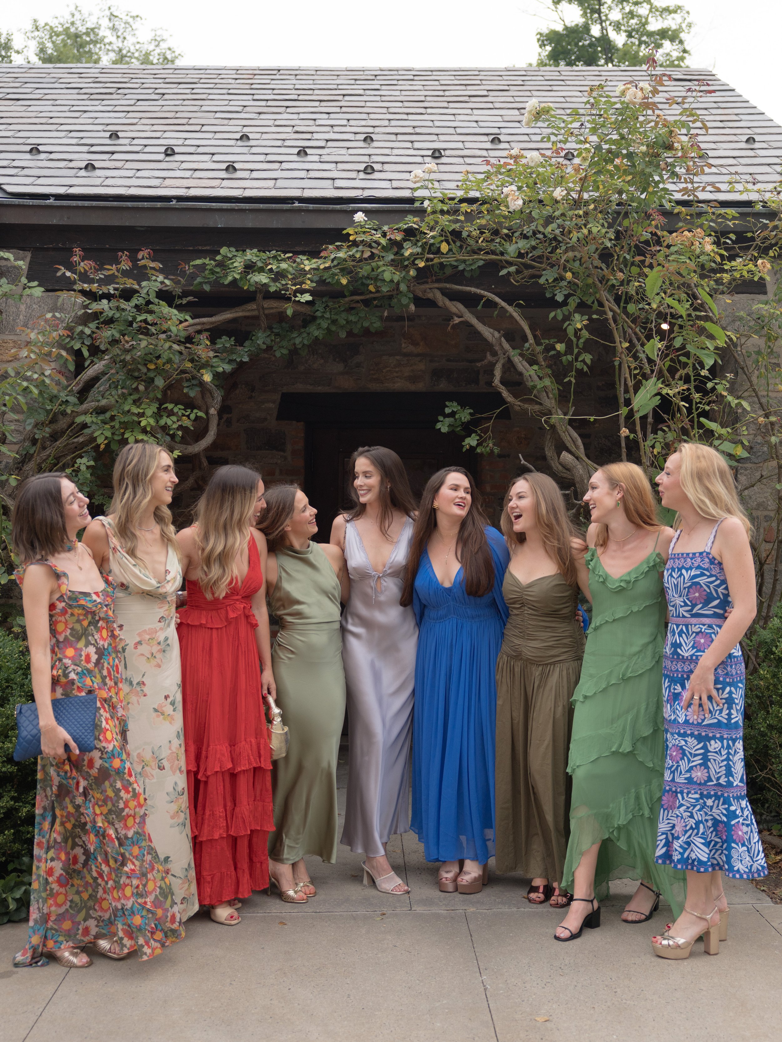 A colorful group of wedding guests gather together for a photograph beneath the natural green branches and stone archways of Blue Hill at Stone Barns. 
