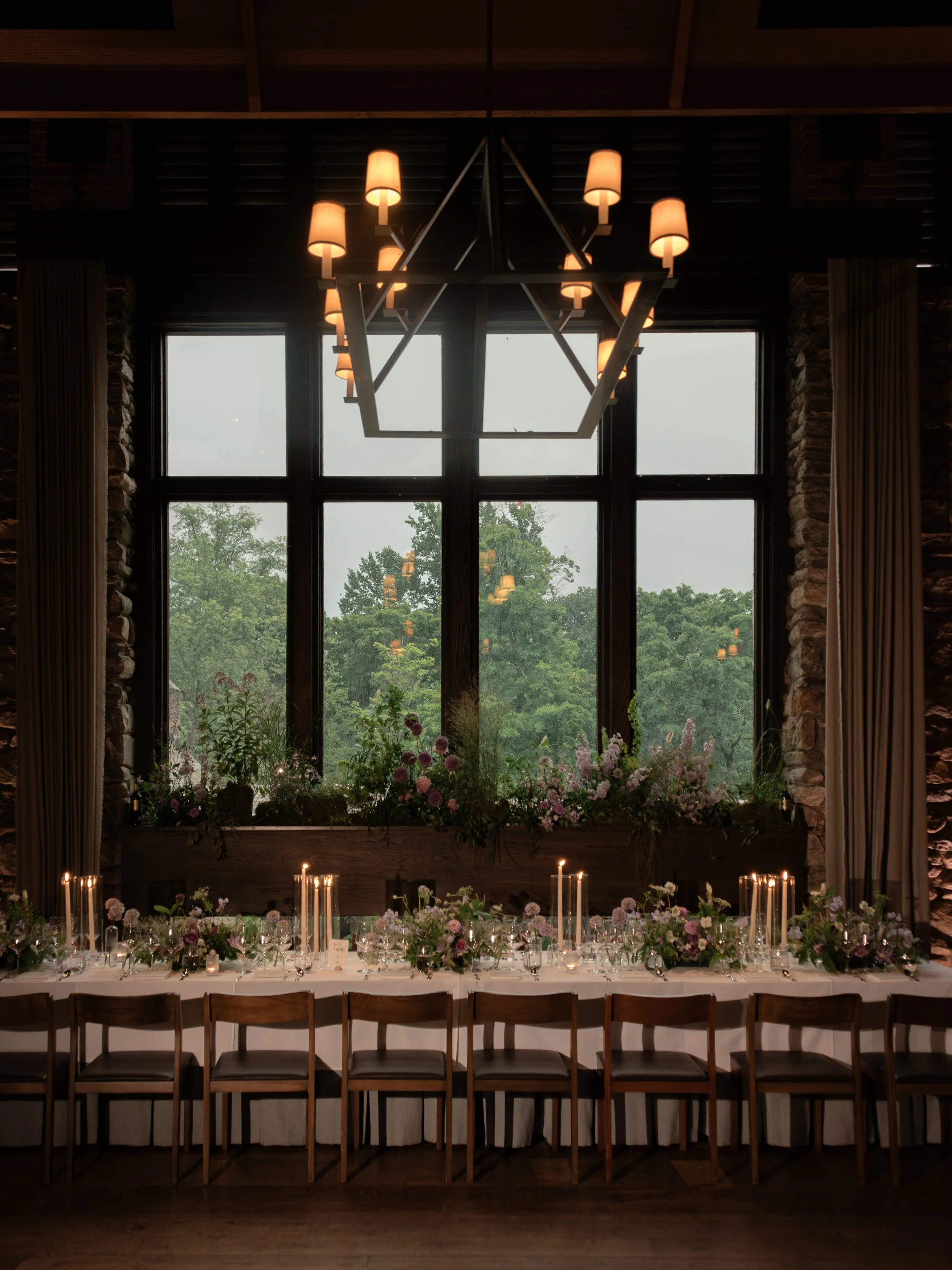 Candlelit wedding table beneath a statement chandelier with summer florals designed by Mudari Creative.