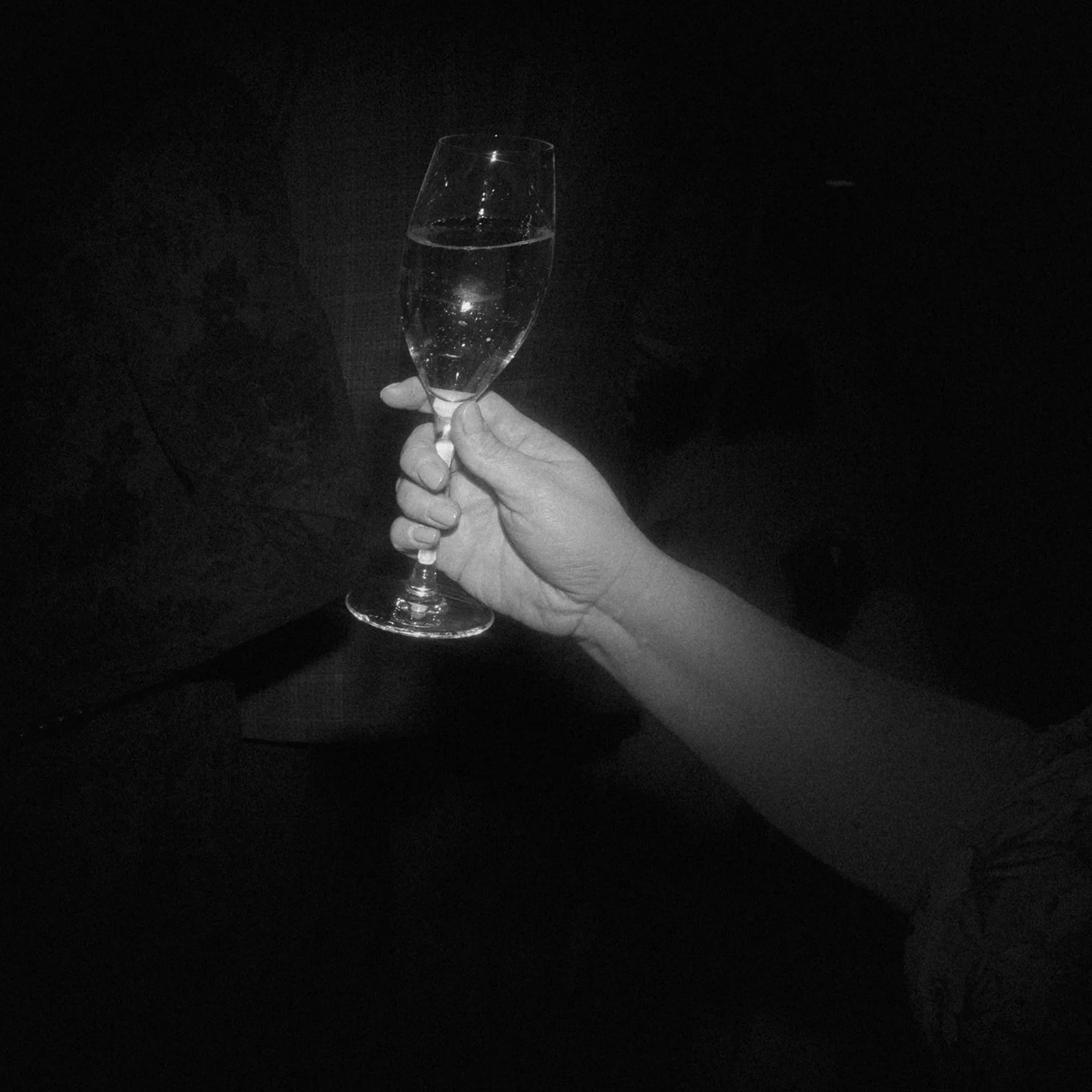 Black-and-white close-up of a hand holding a champagne glass during a wedding reception.